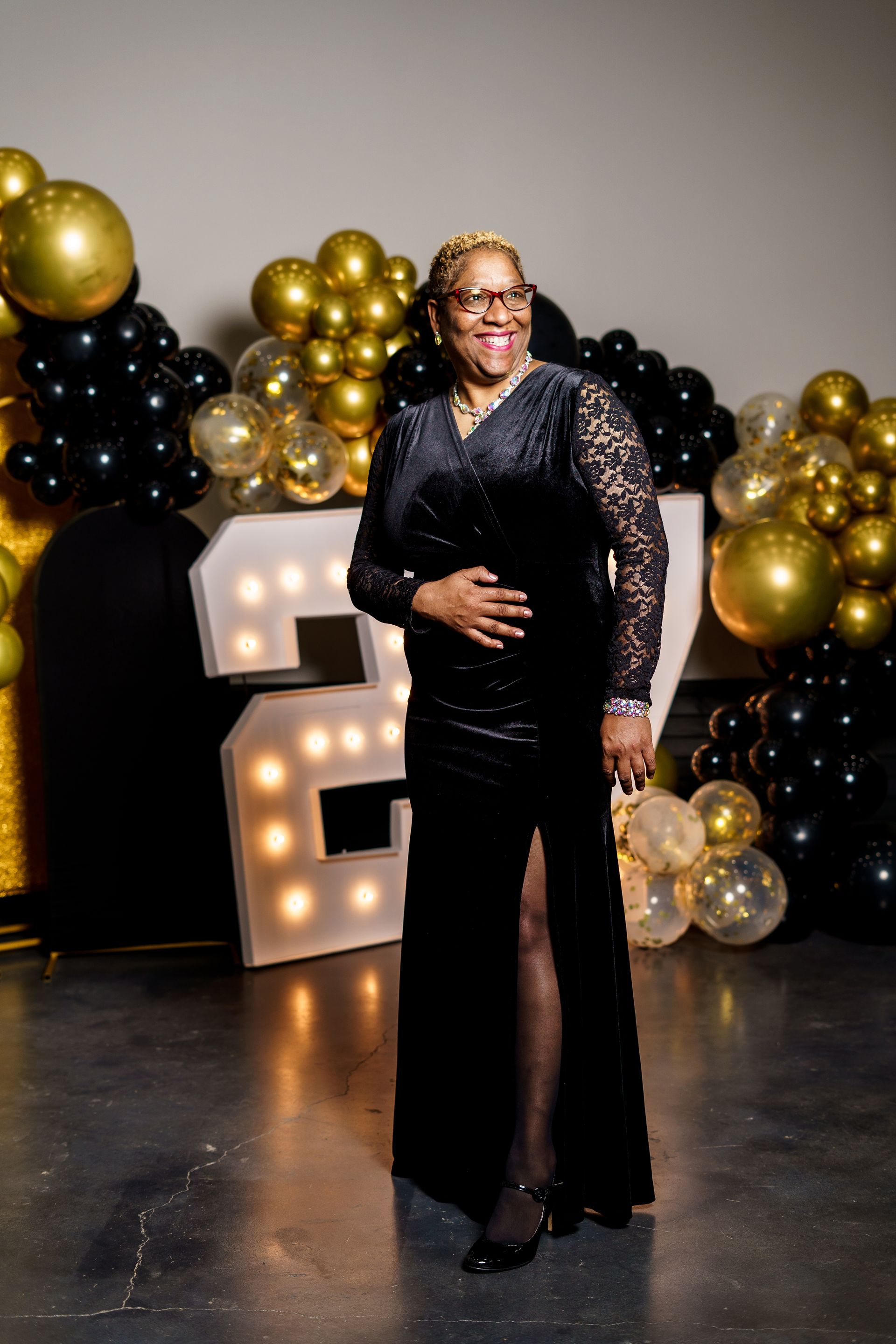A woman in a black dress is standing in front of balloons.