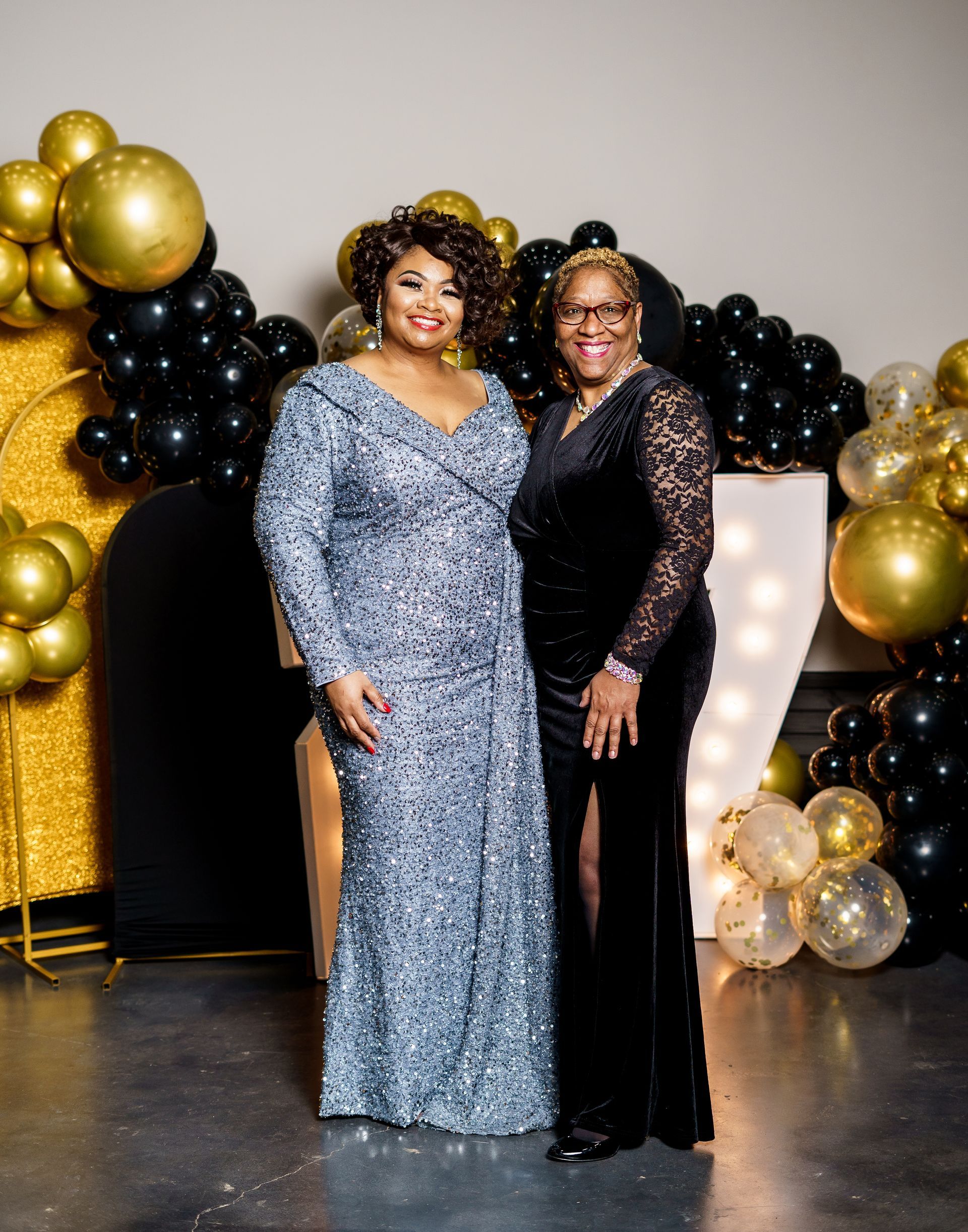 Two women in dresses are standing next to each other in front of balloons.