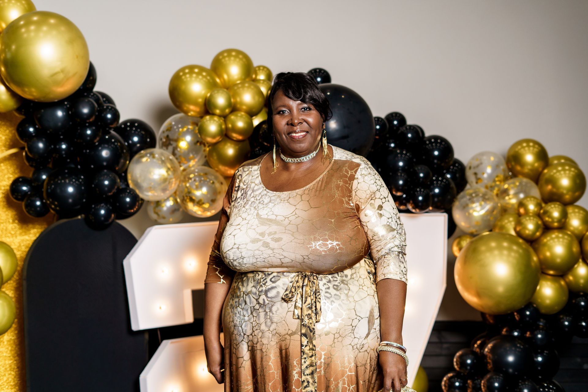 A woman in a gold dress is standing in front of balloons.