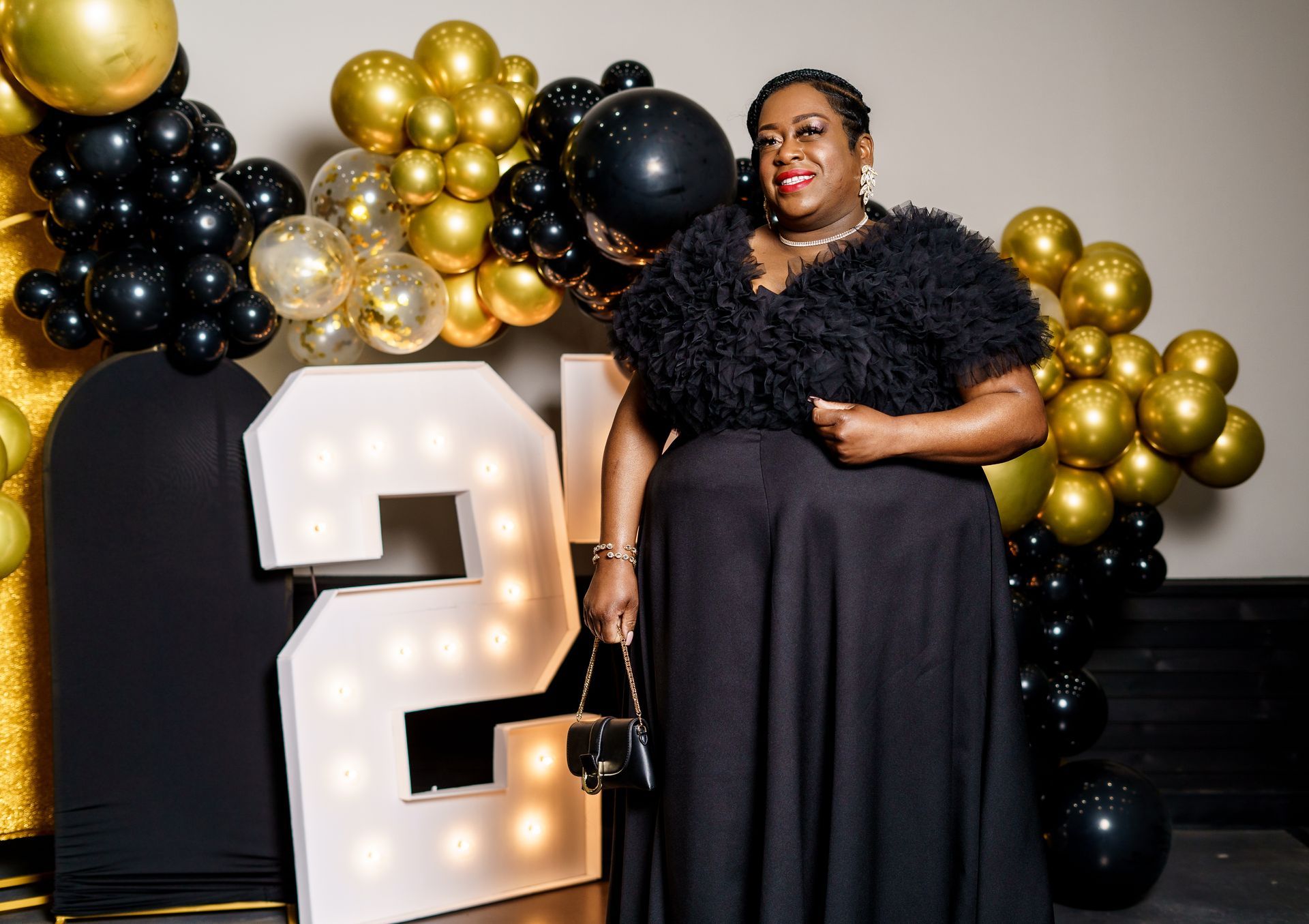 A woman in a black dress is standing in front of balloons and a large number.