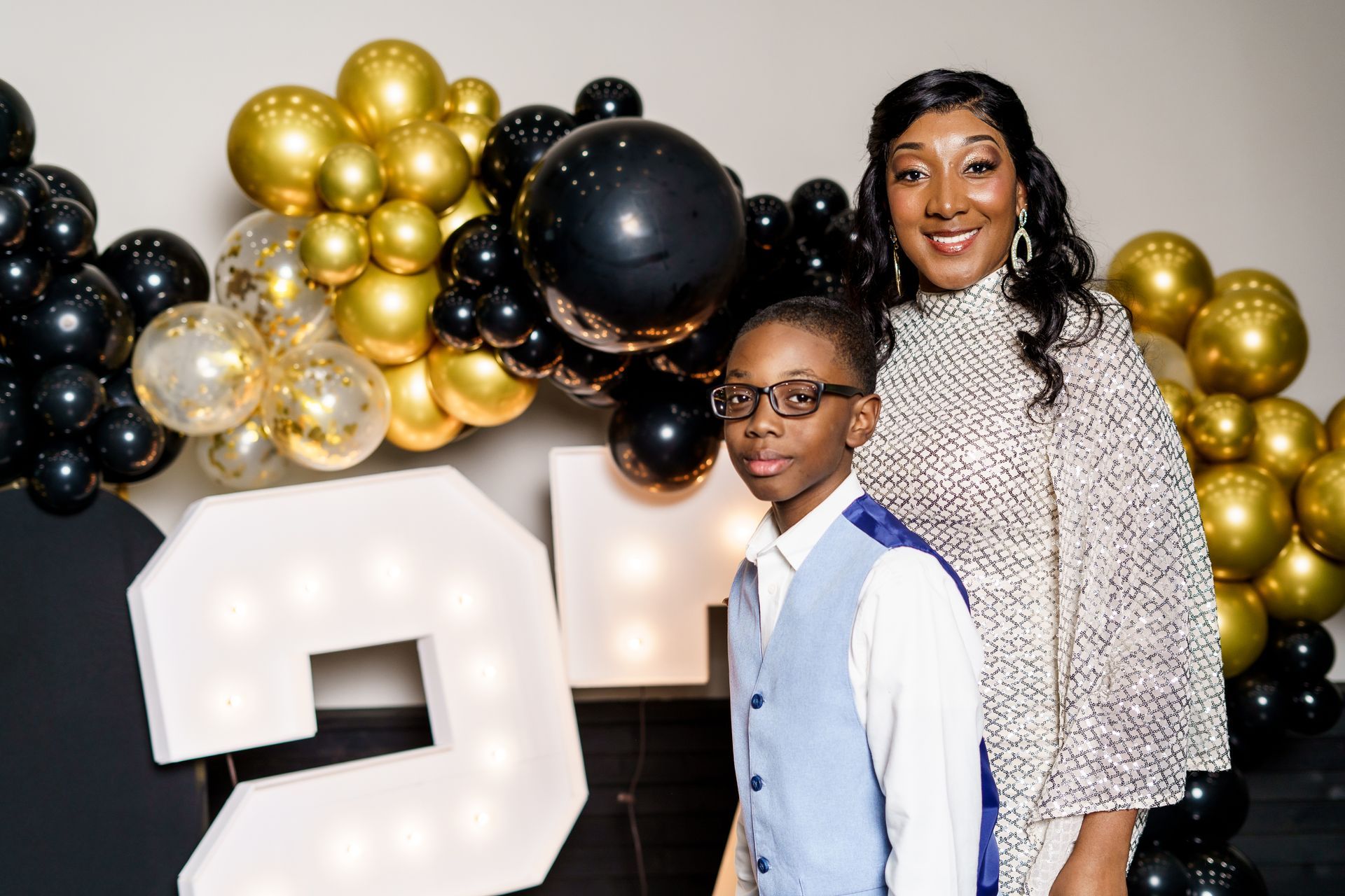 A woman and a boy are posing for a picture in front of balloons.