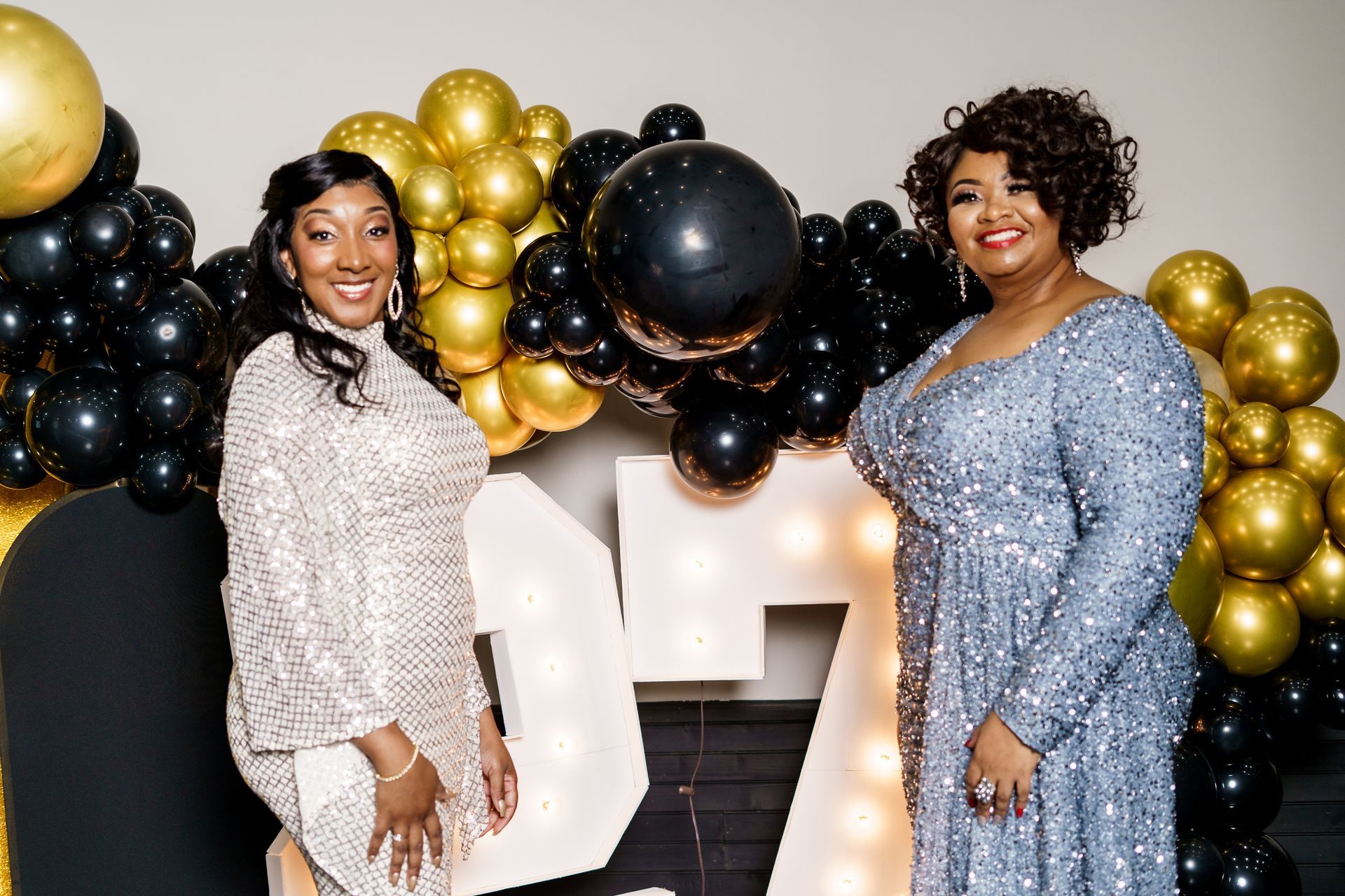Two women are standing next to each other in front of balloons.