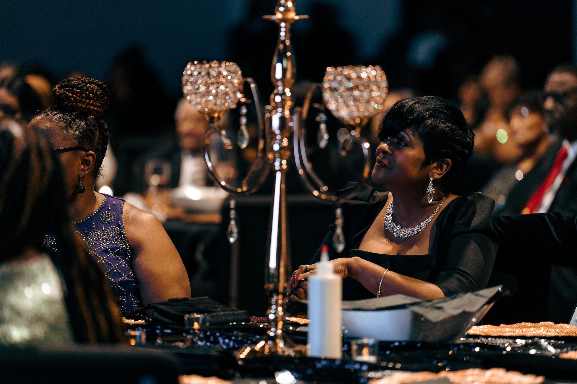 A woman in a black dress is sitting at a table with other people.