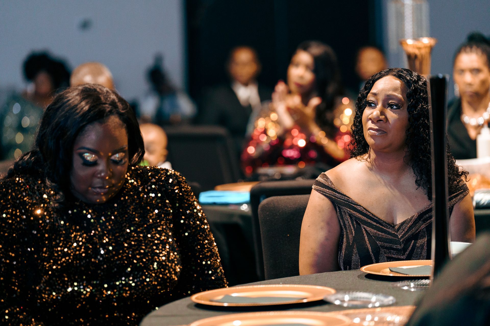 Two women are sitting at a table with plates on it.
