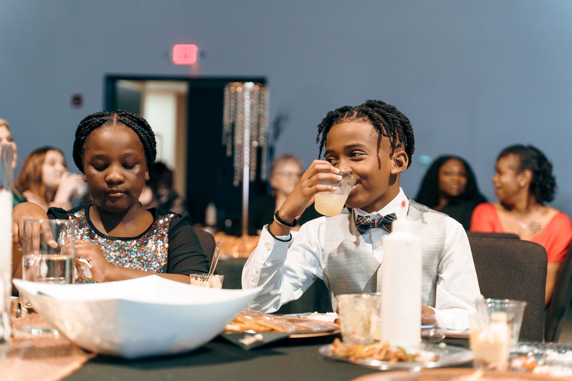 A boy and a girl are sitting at a table drinking from glasses.
