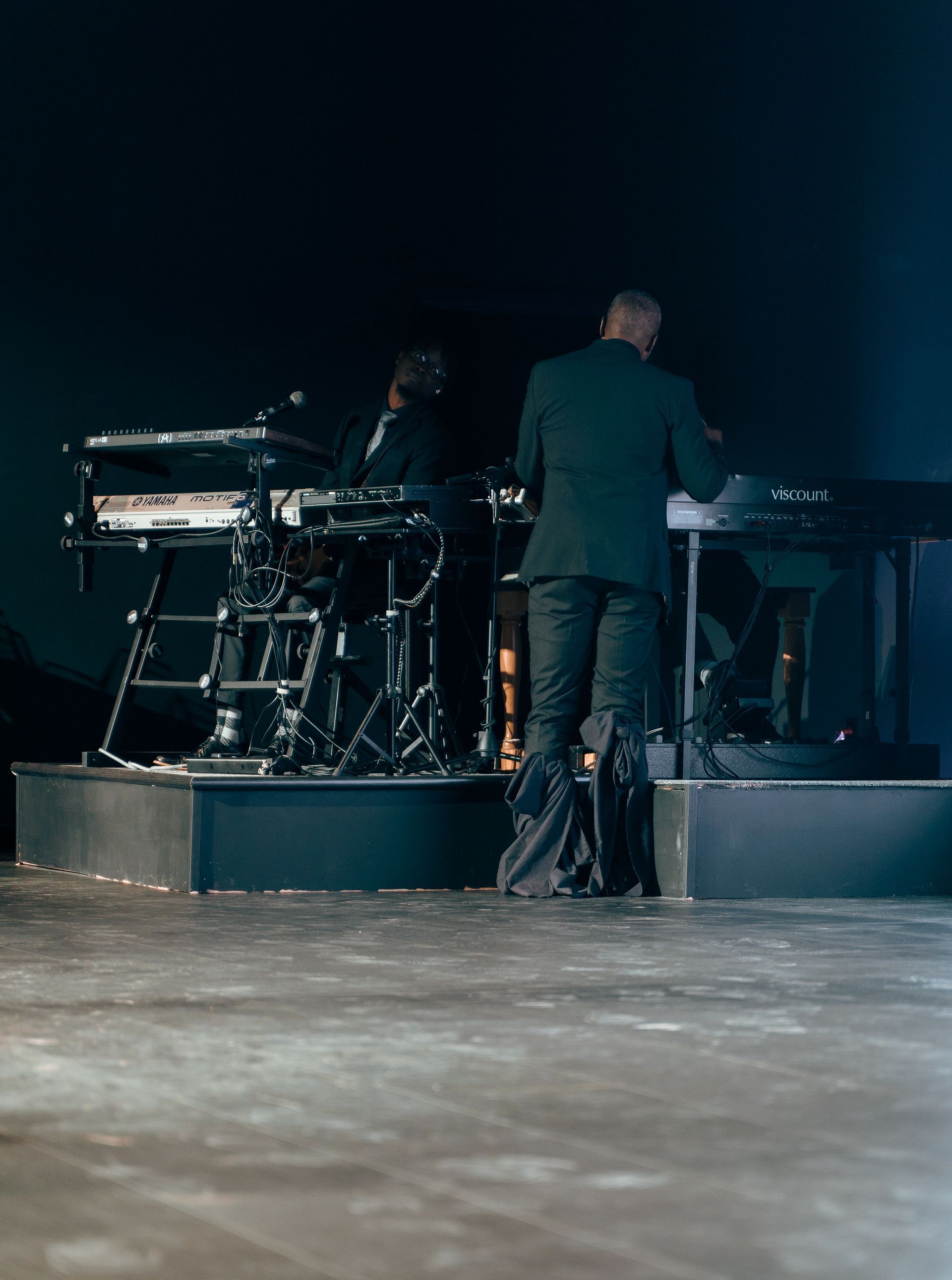 A man in a suit is standing on a stage in front of a keyboard.