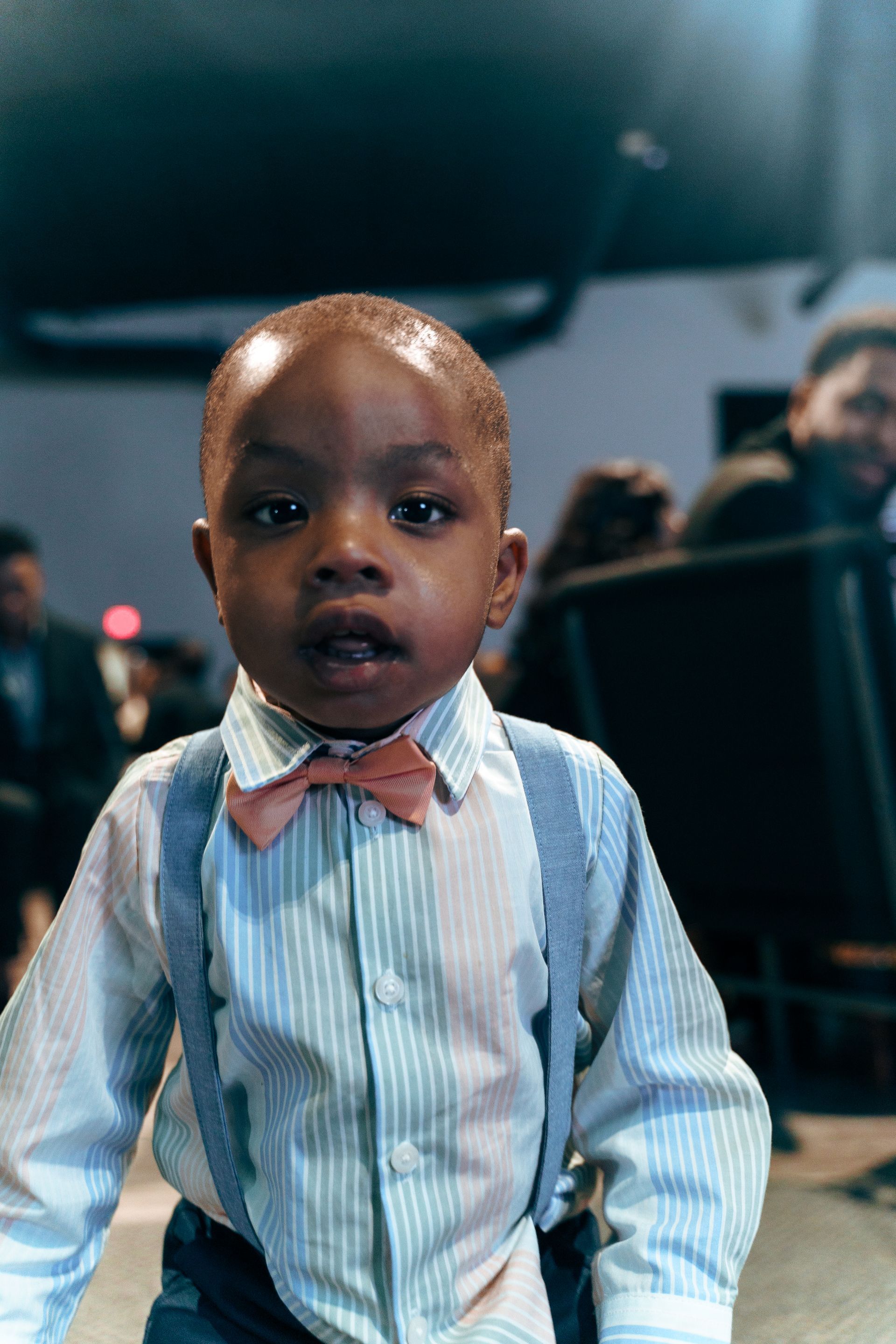 A young boy wearing a bow tie and suspenders is looking at the camera.