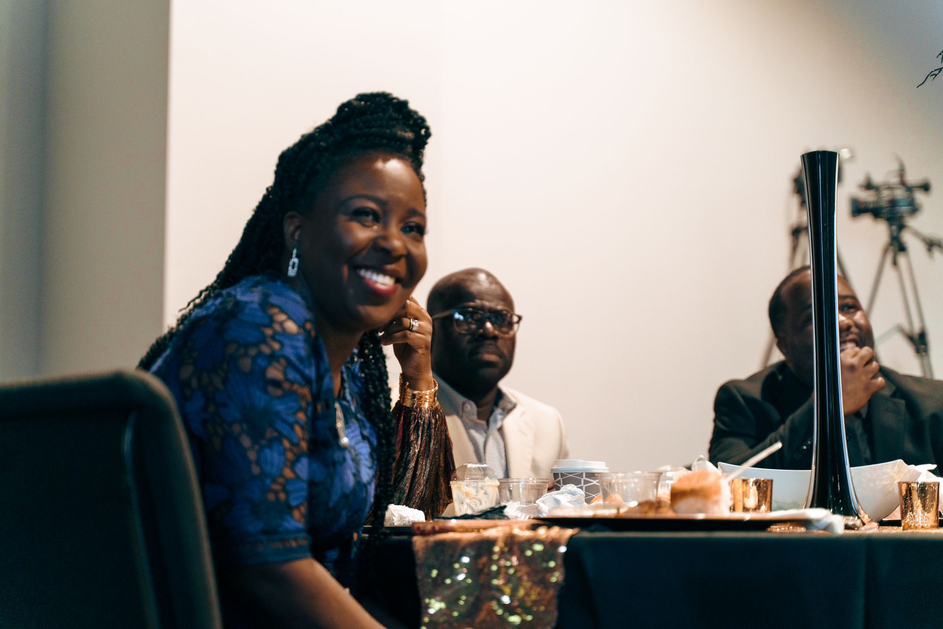A woman is smiling while sitting at a table with other people.