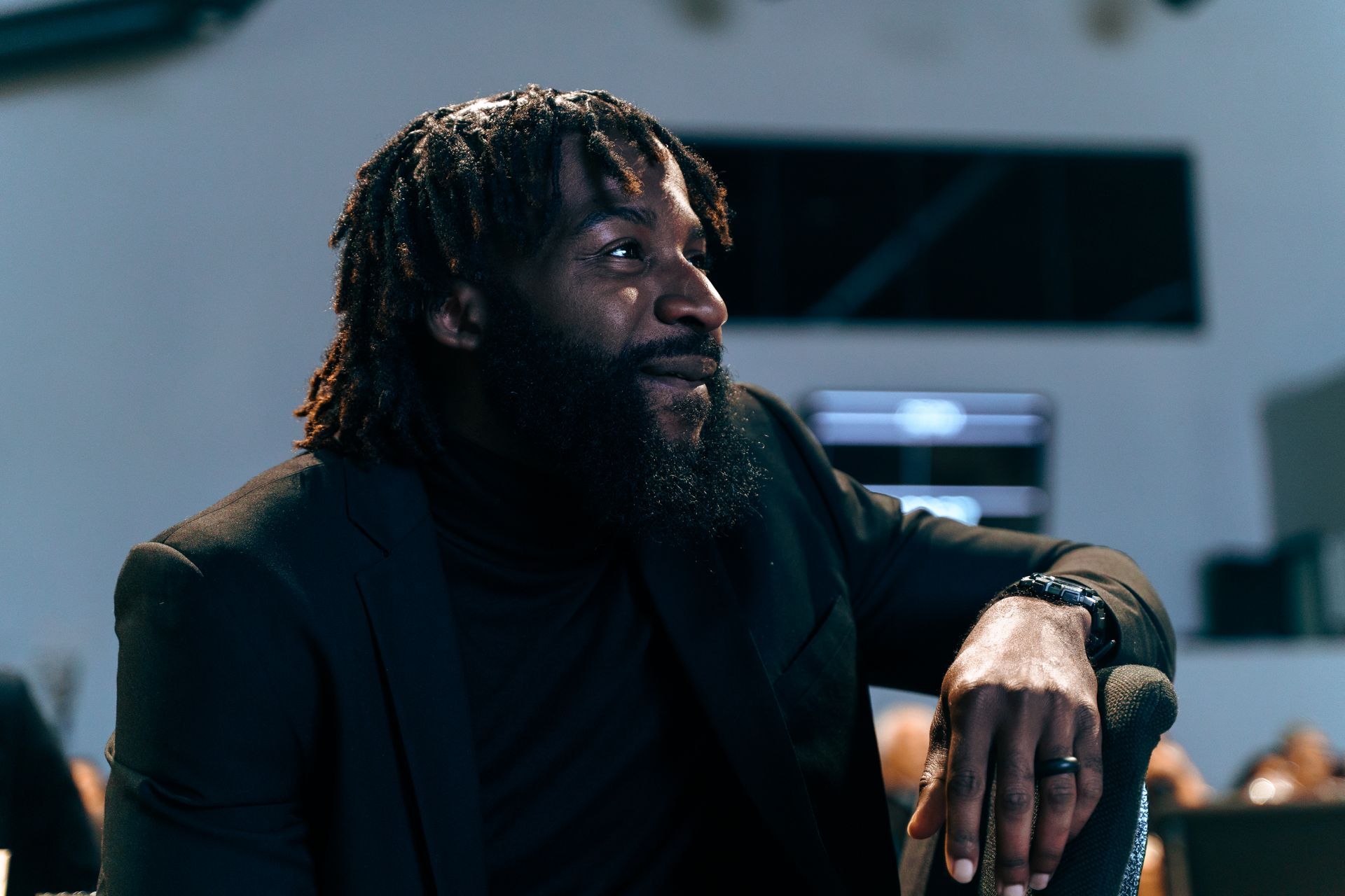 A man with dreadlocks and a beard is sitting with his hand on his knee.