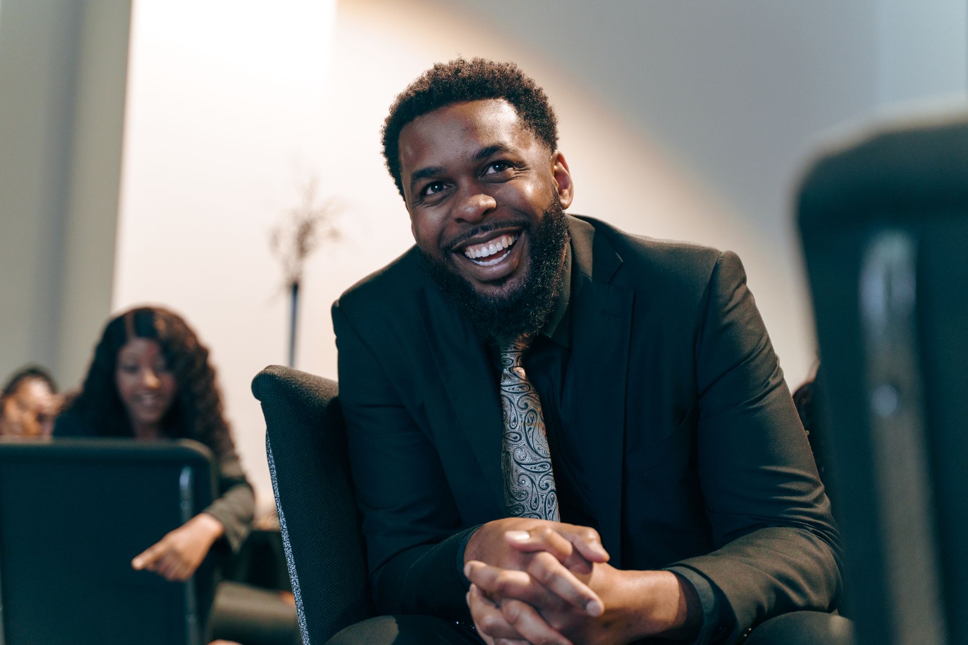 A man in a suit and tie is sitting in a chair and smiling.
