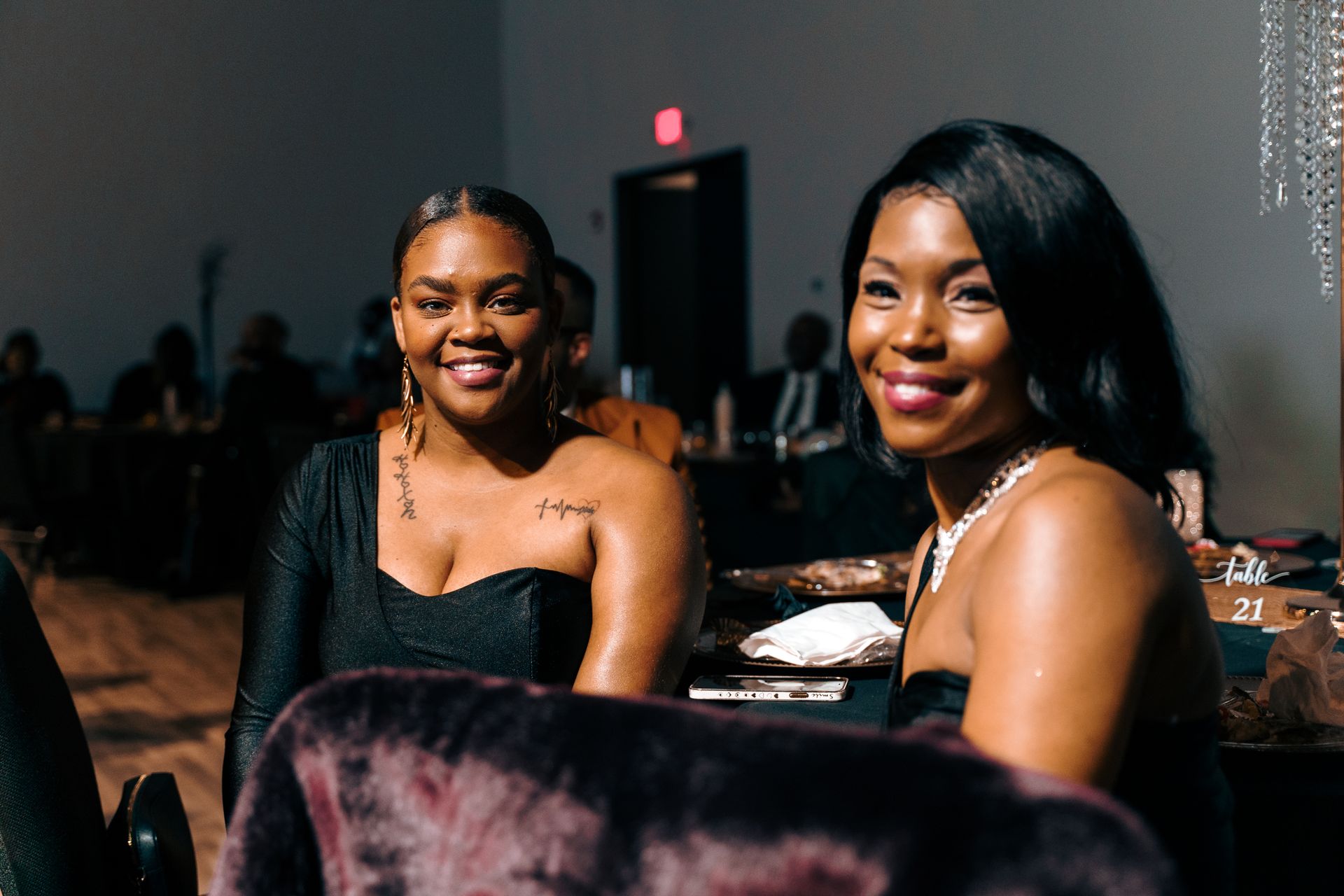 Two women are sitting next to each other in a chair at a party.