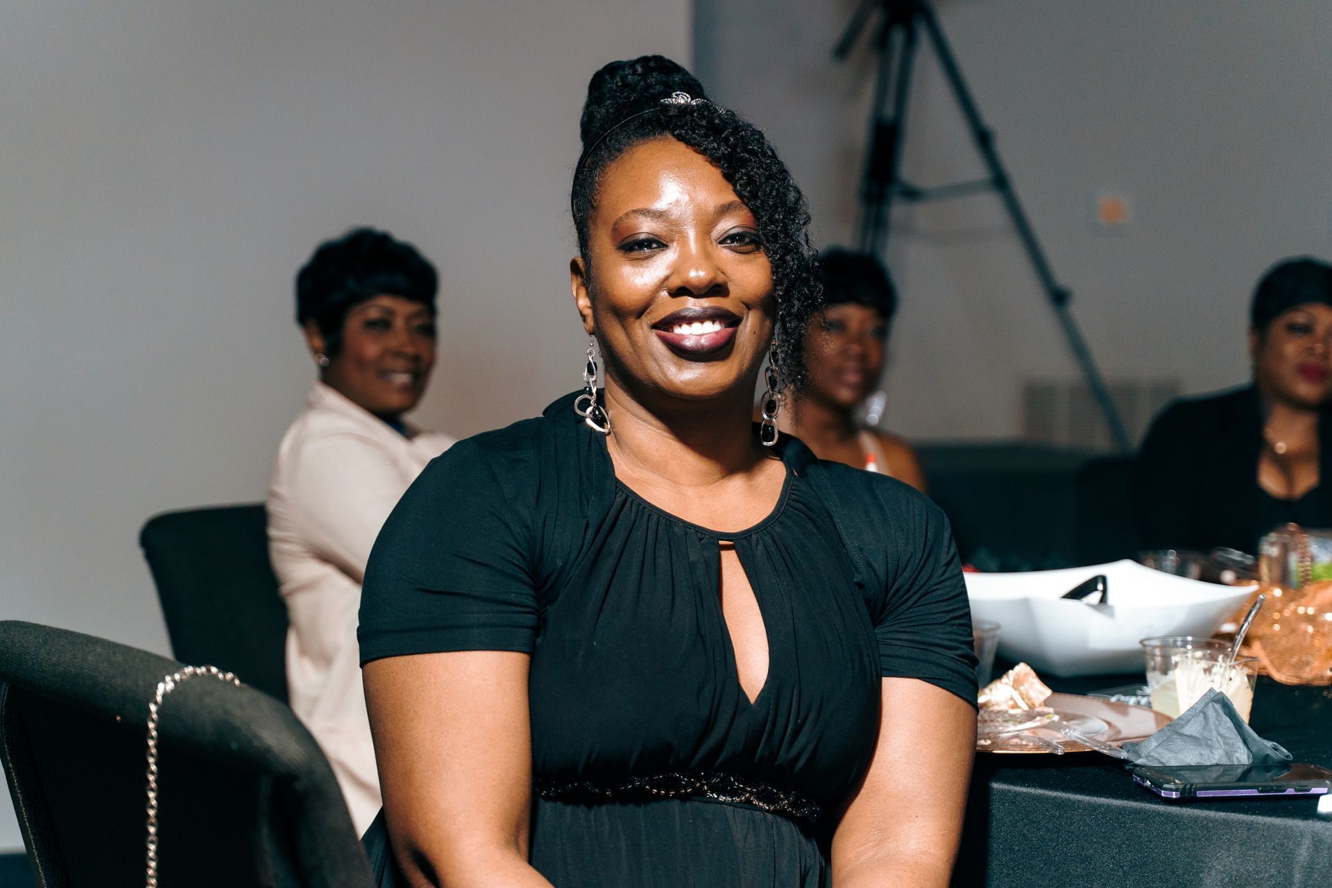 A woman in a black dress is sitting at a table with other women.