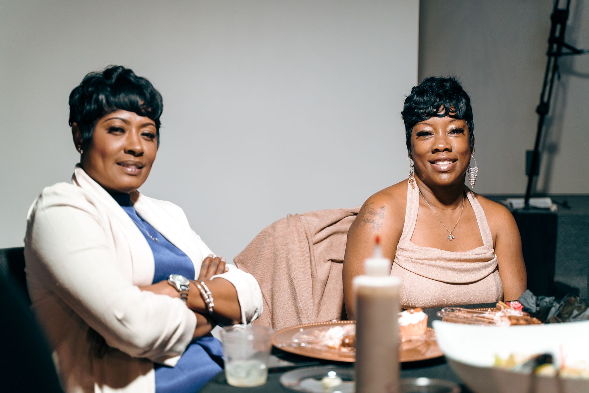 Two women are sitting at a table with their arms crossed.