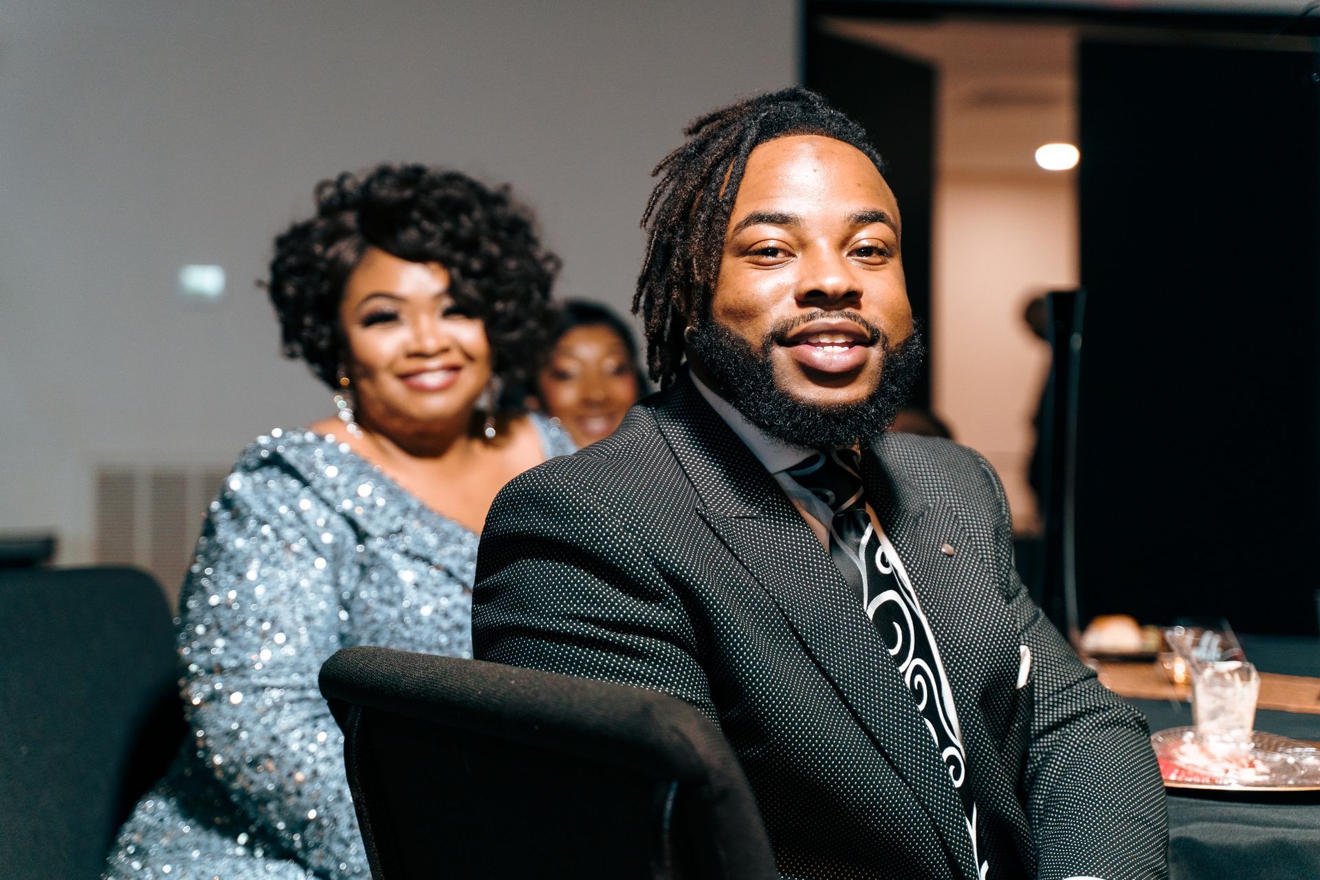 A man in a suit is sitting in a chair next to a woman in a dress.