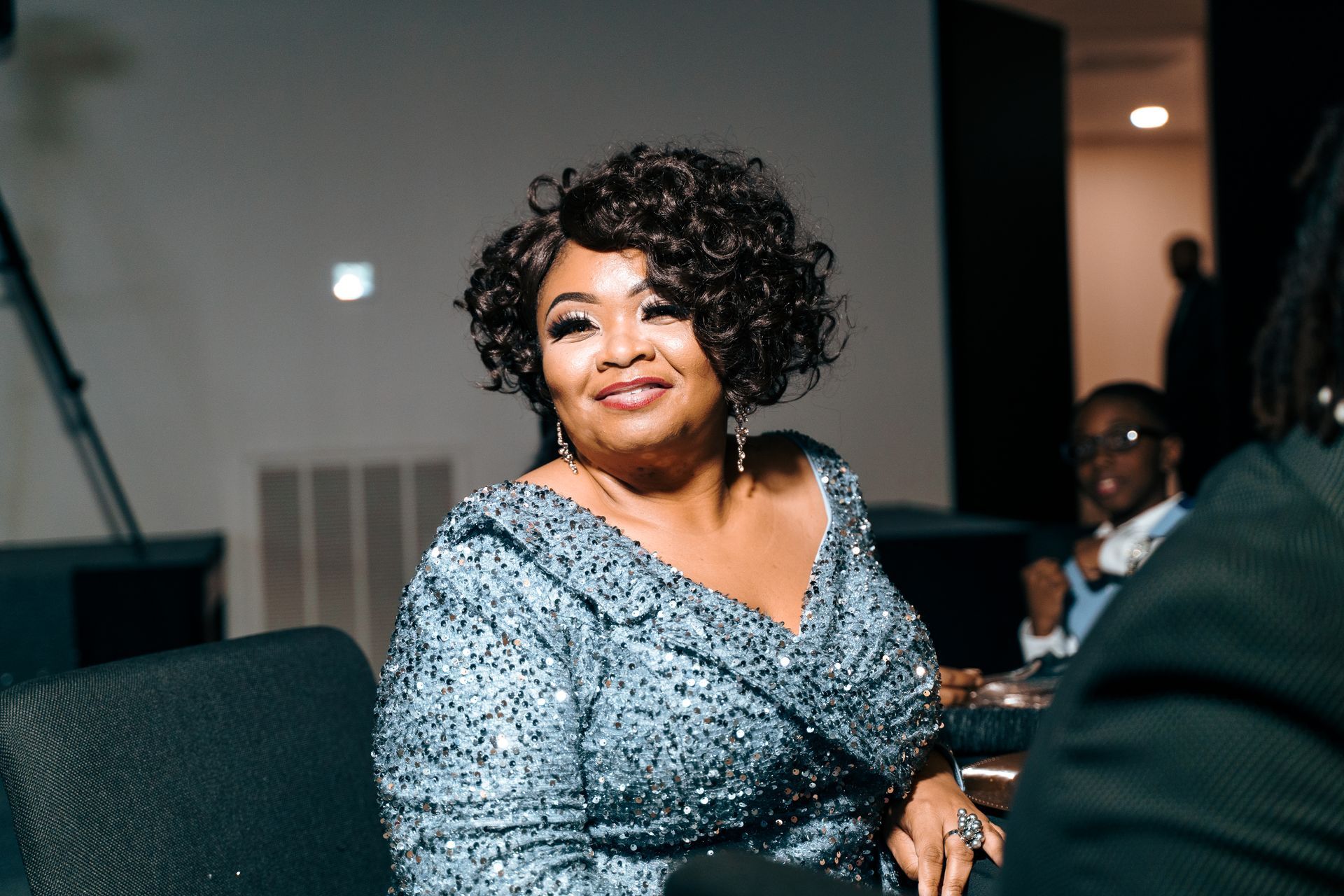 A woman in a gray dress is sitting in a chair and smiling.