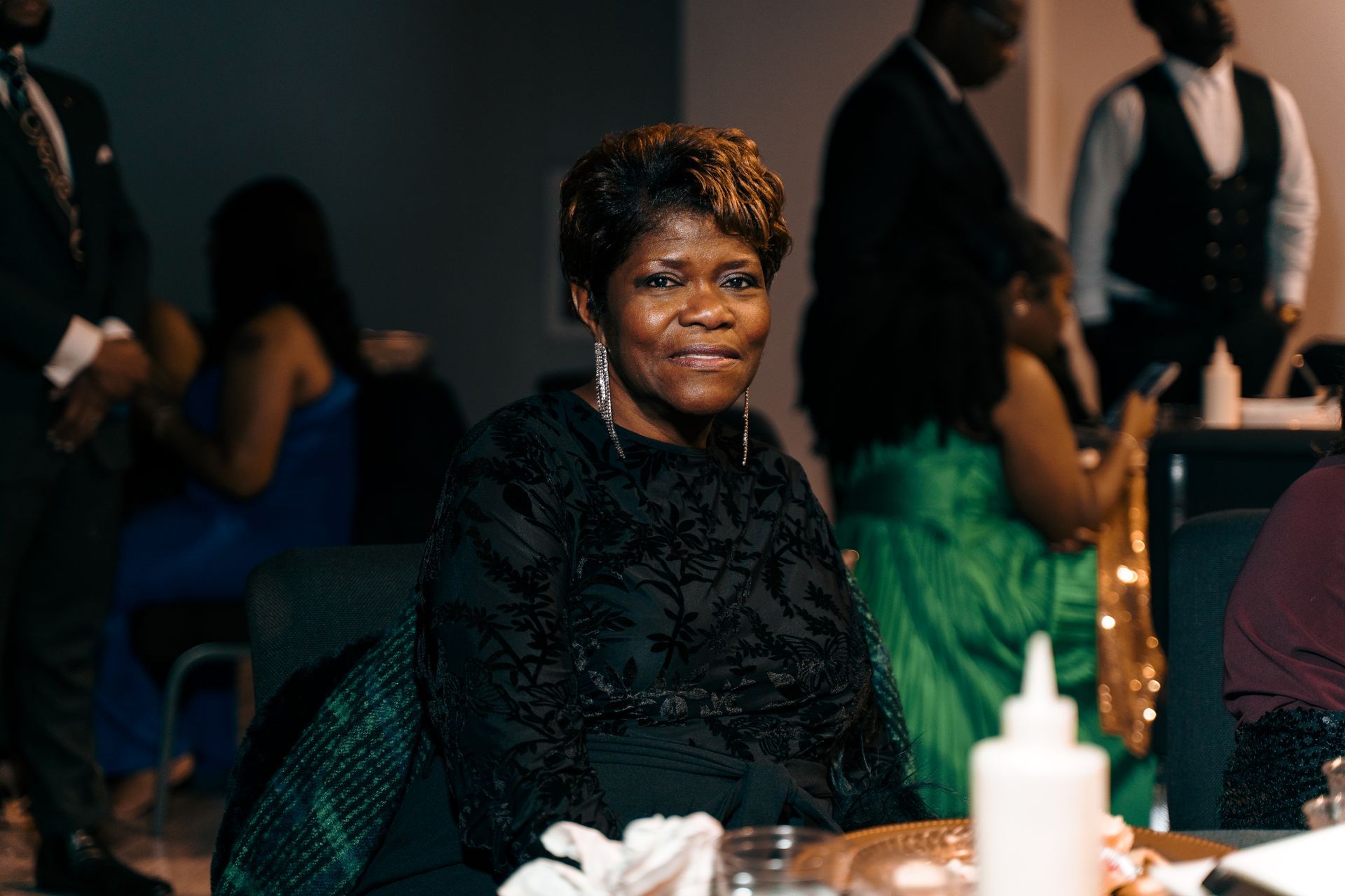 A woman in a black dress is sitting at a table at a party.