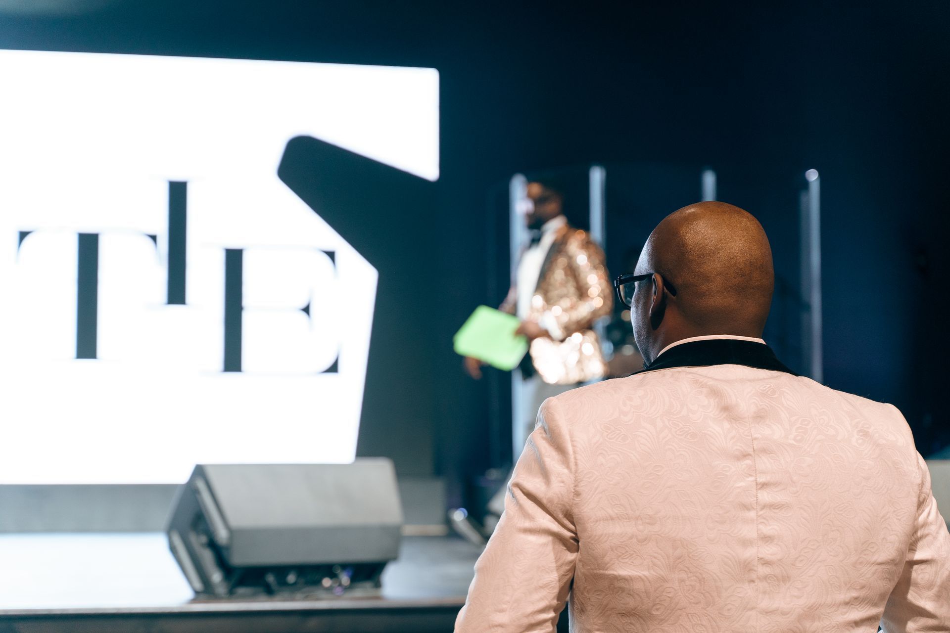 A man is sitting in front of a large screen with the word the on it.