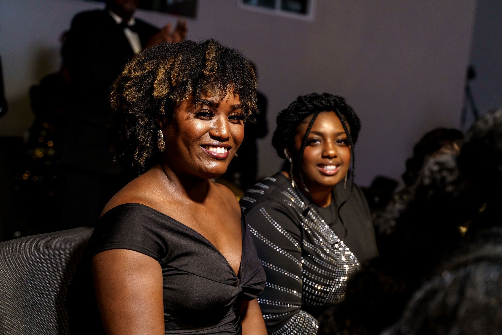 Two women are sitting next to each other in a room and smiling.