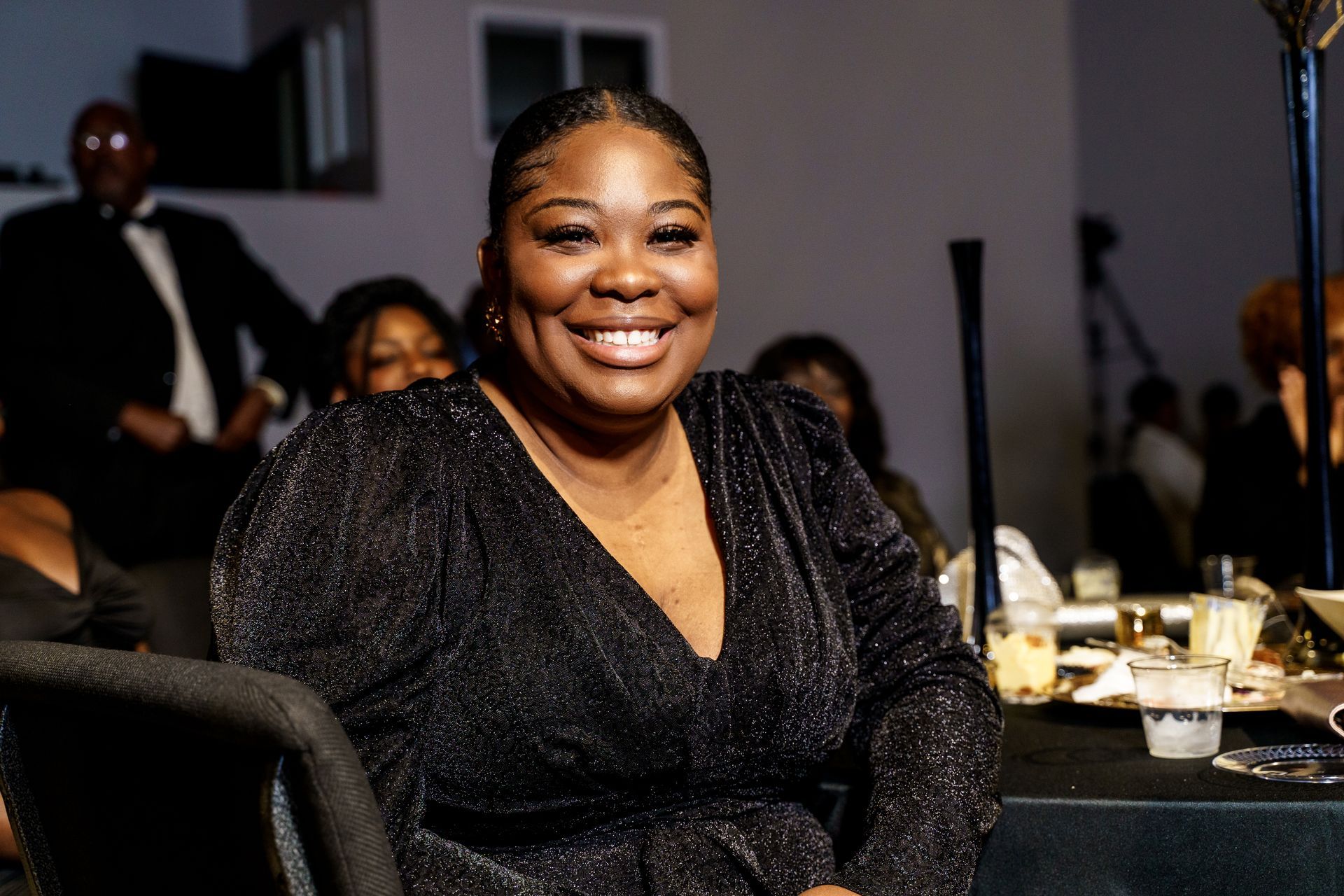 A woman in a black dress is smiling while sitting at a table.