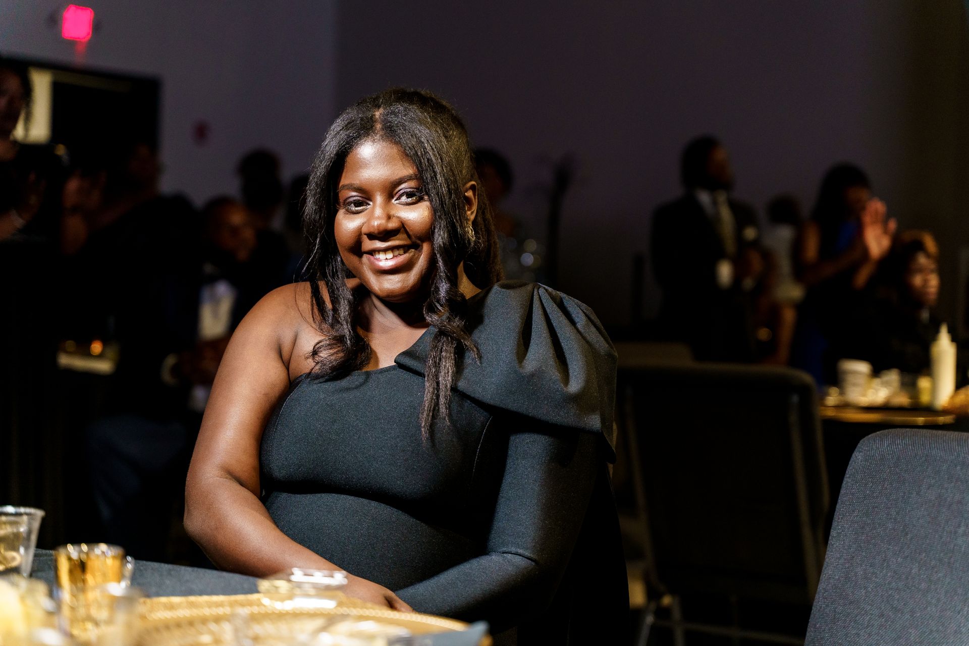 A woman in a black dress is sitting at a table in a dark room.