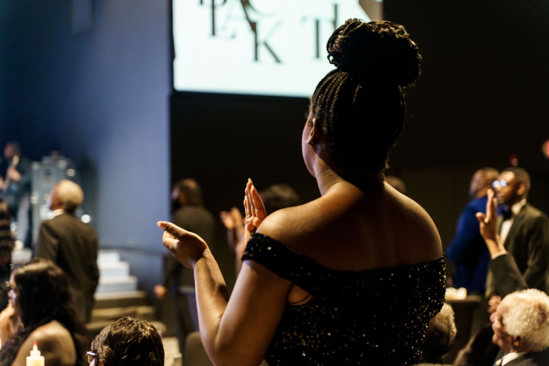 A woman in a black dress is clapping in front of a crowd