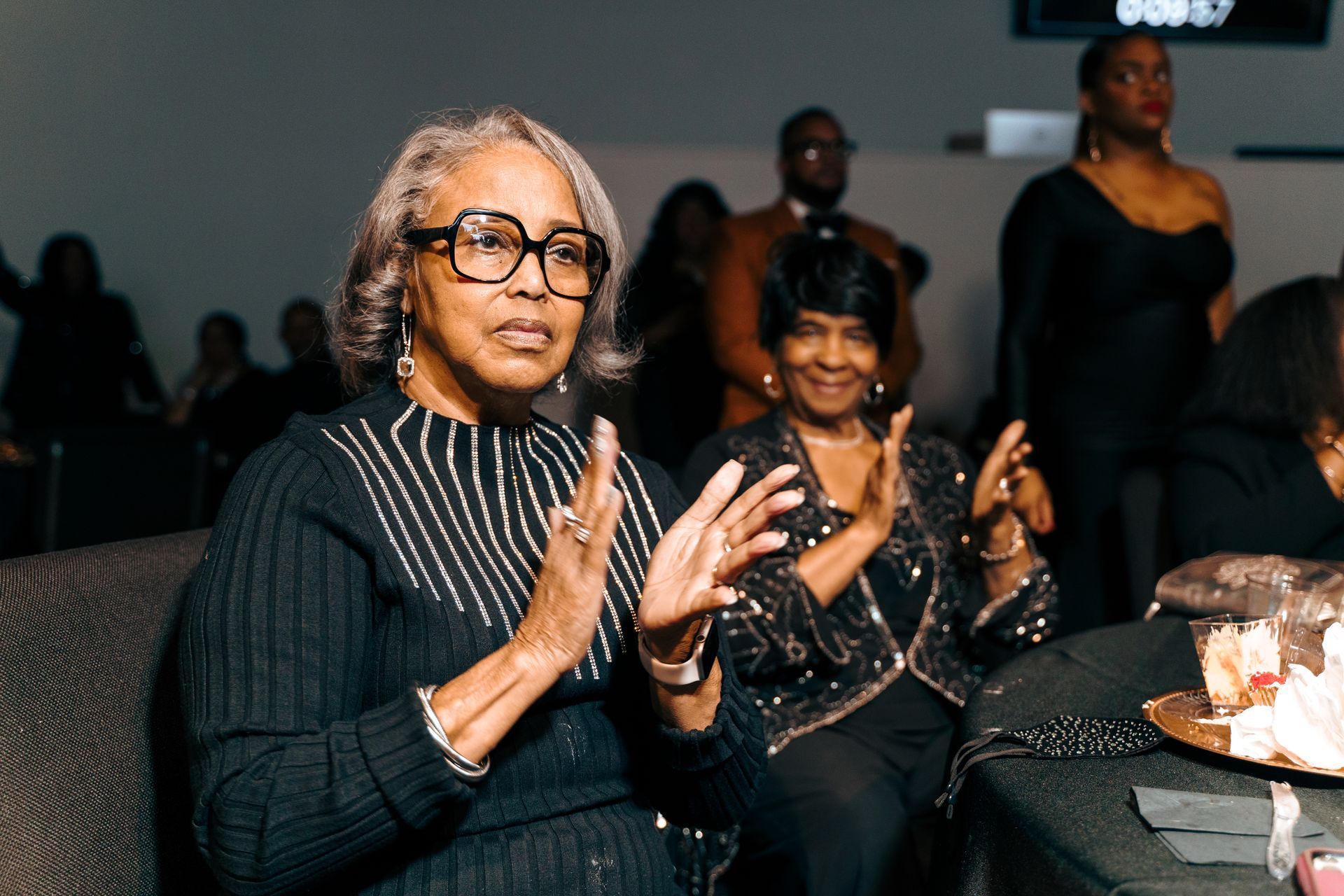 A woman wearing glasses is sitting on a couch applauding.