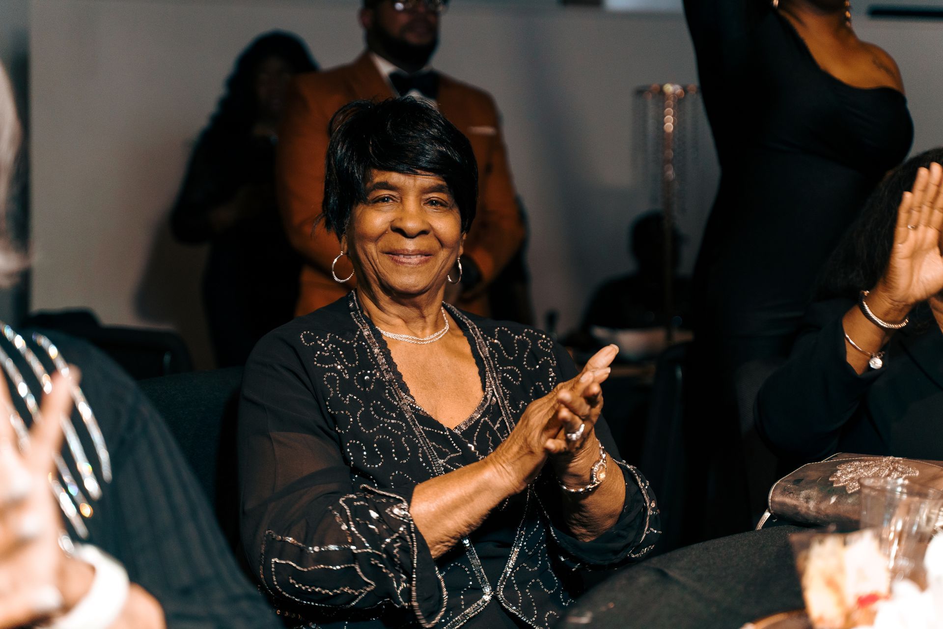 A woman in a black dress is sitting at a table clapping her hands.
