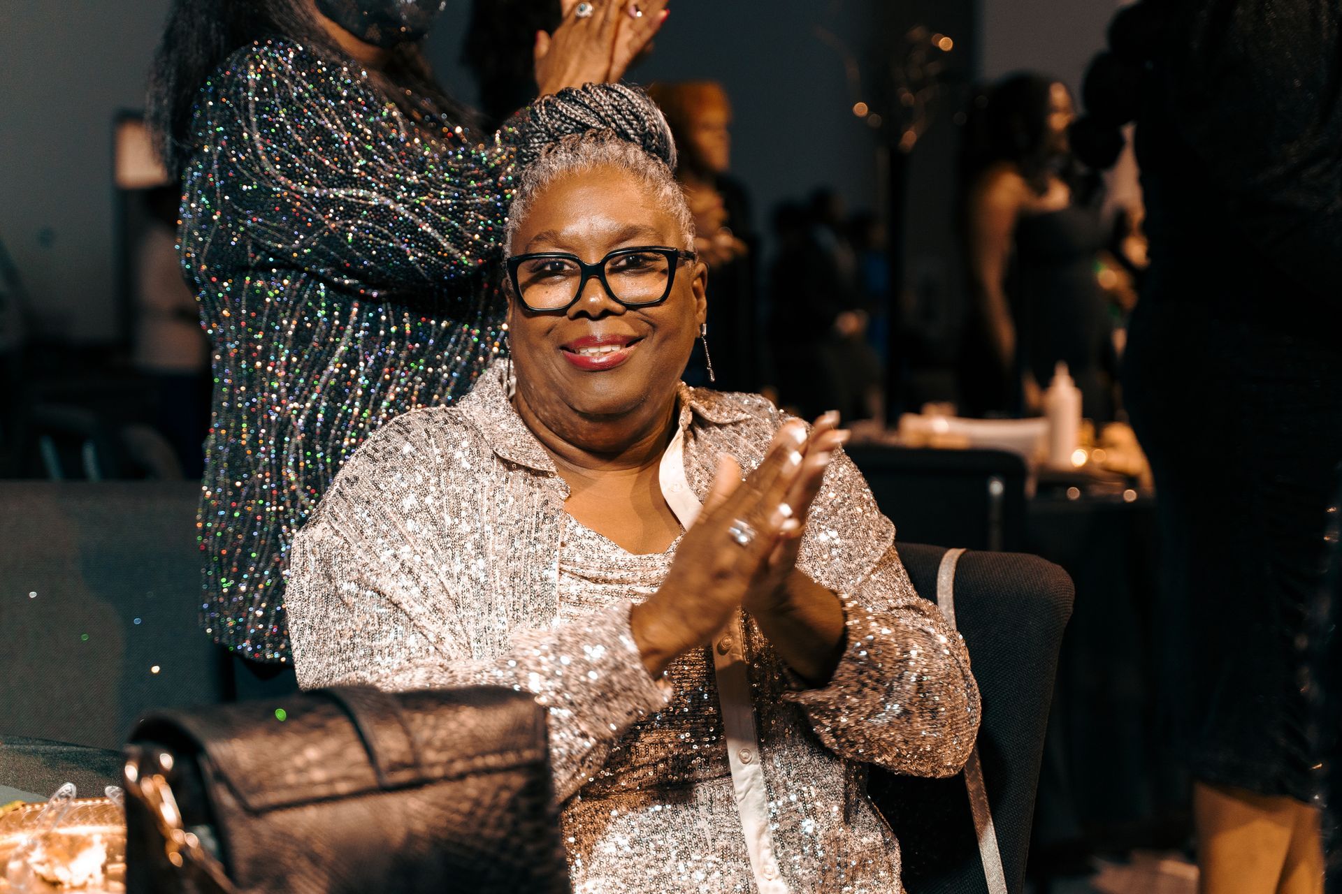 A woman in a sequined dress is sitting in a chair and clapping her hands.
