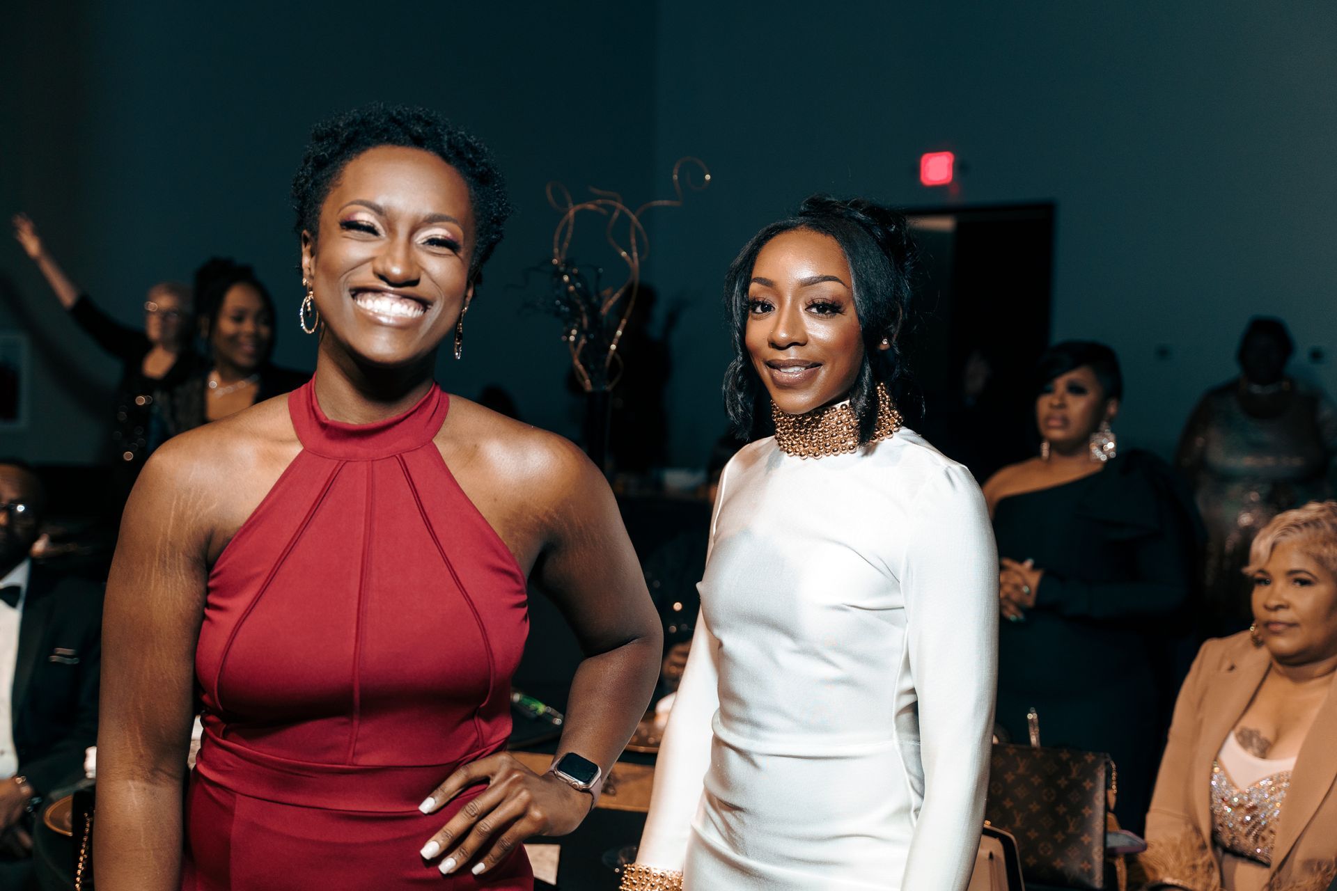 Two women are standing next to each other at a party and smiling.