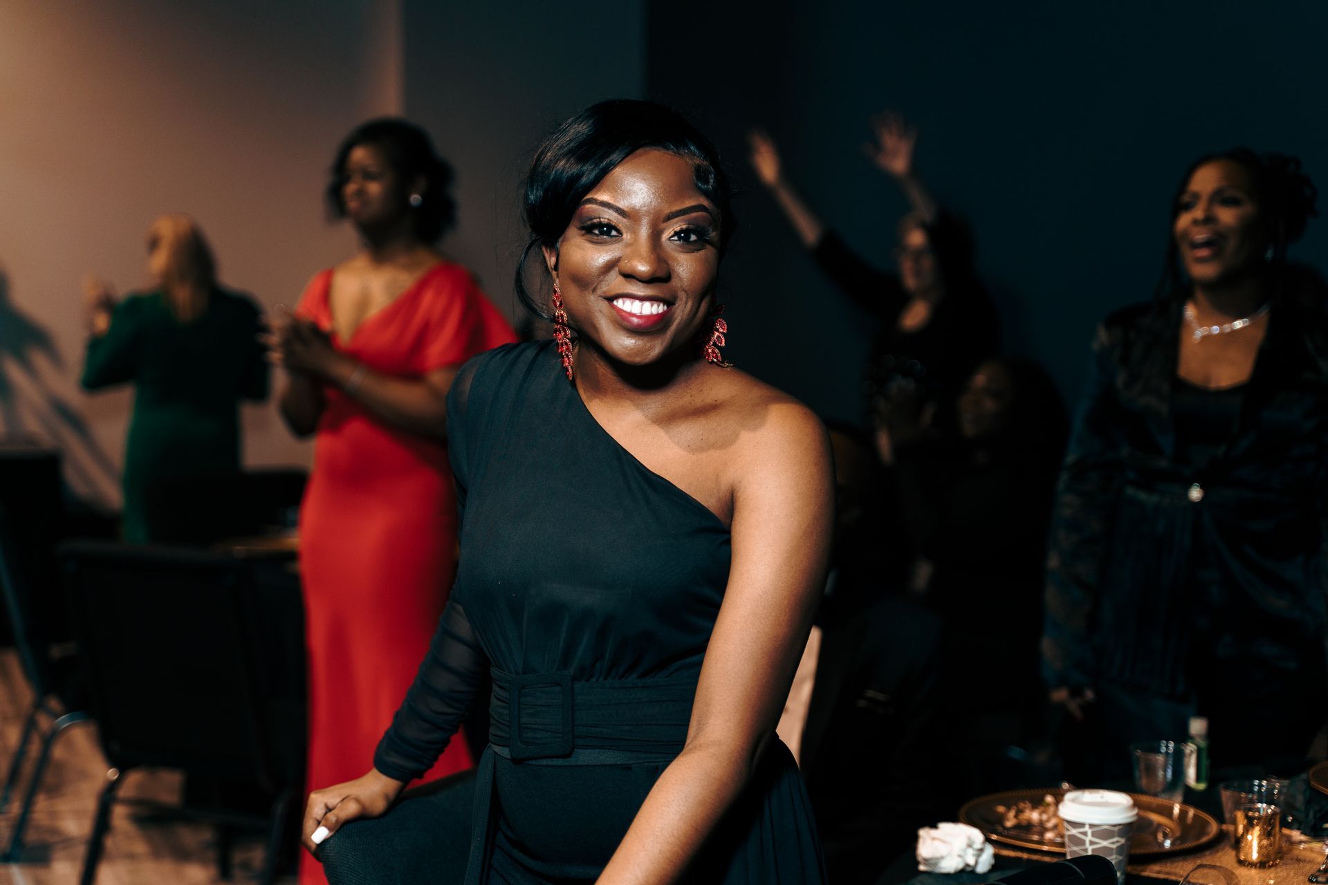 A woman in a black dress is posing for a picture at a party.