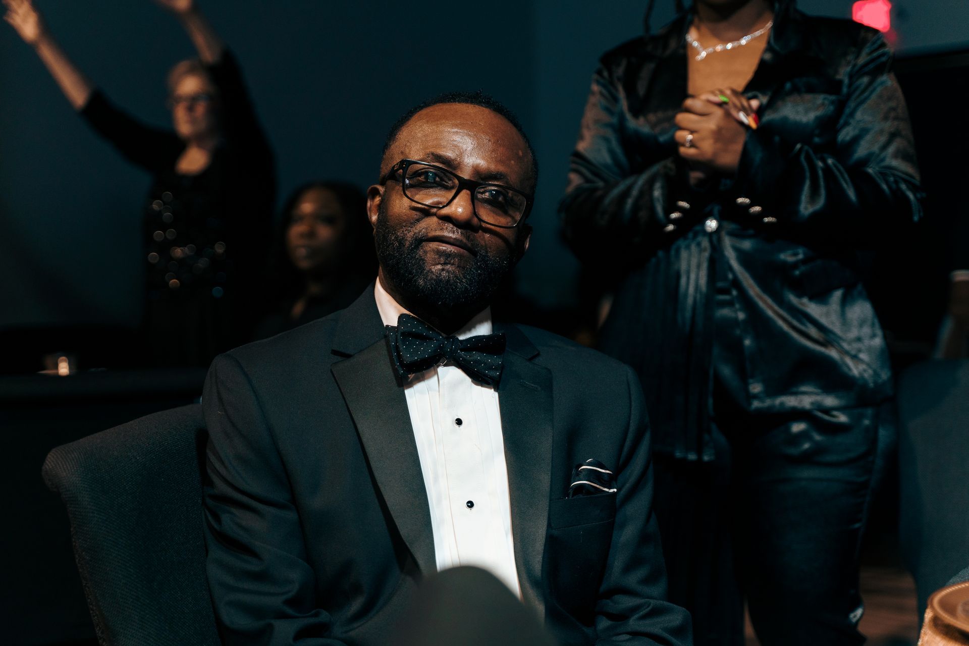 A man in a tuxedo and bow tie is sitting in a chair.