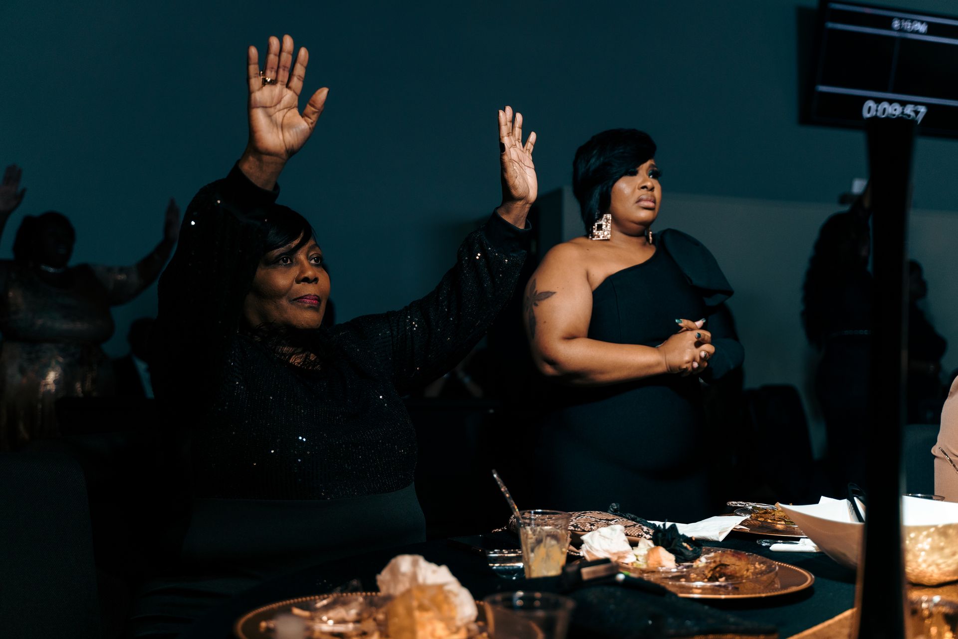 Two women are sitting at a table with their hands in the air.