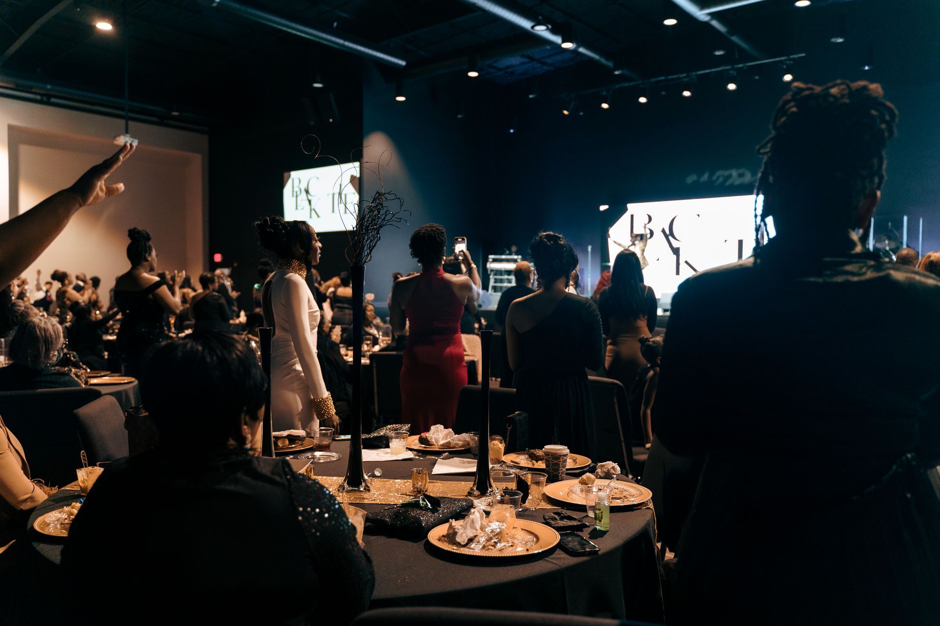 A group of people are sitting at tables in a dark room.