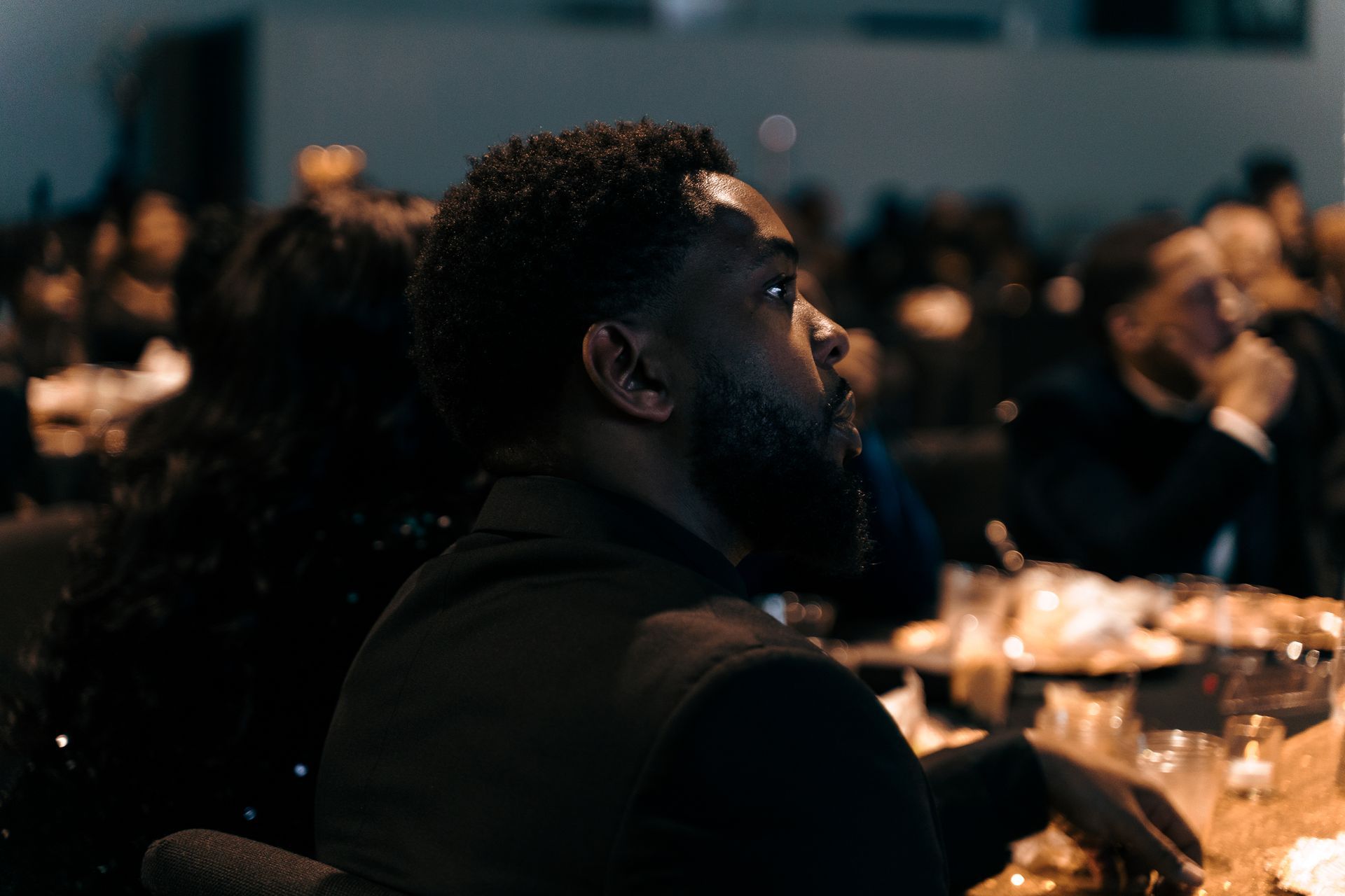 A man with a beard is sitting at a table in a dark room.