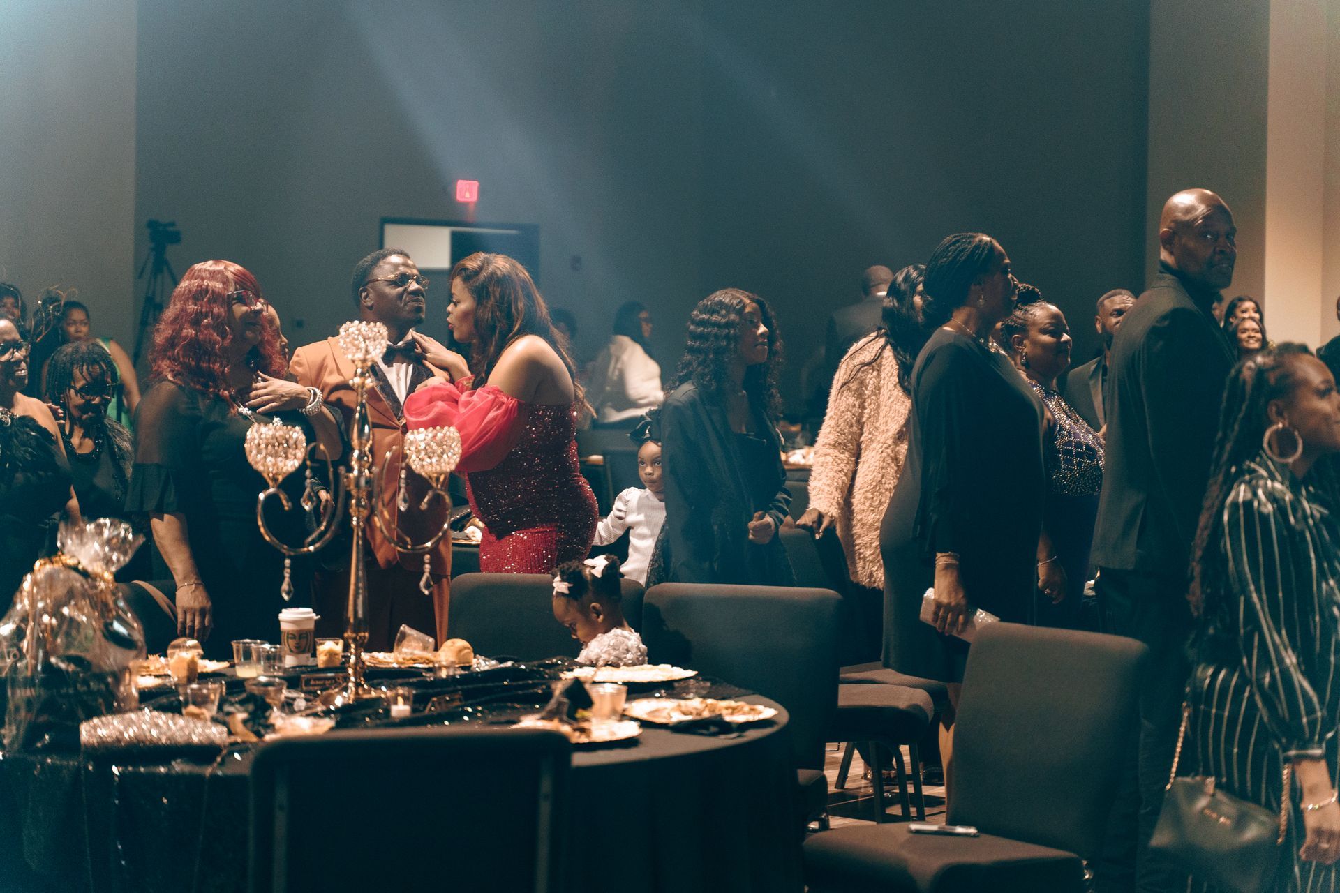 A large group of people are standing around tables at a party.