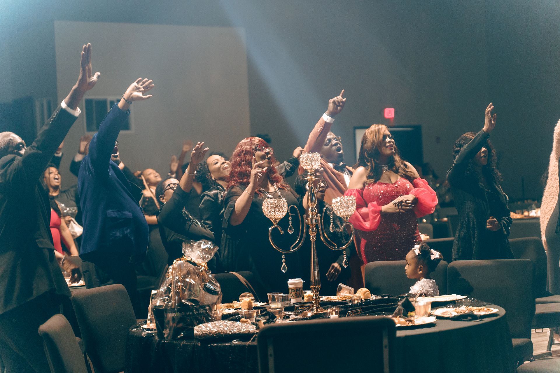 A group of people are sitting at a table with their arms in the air.