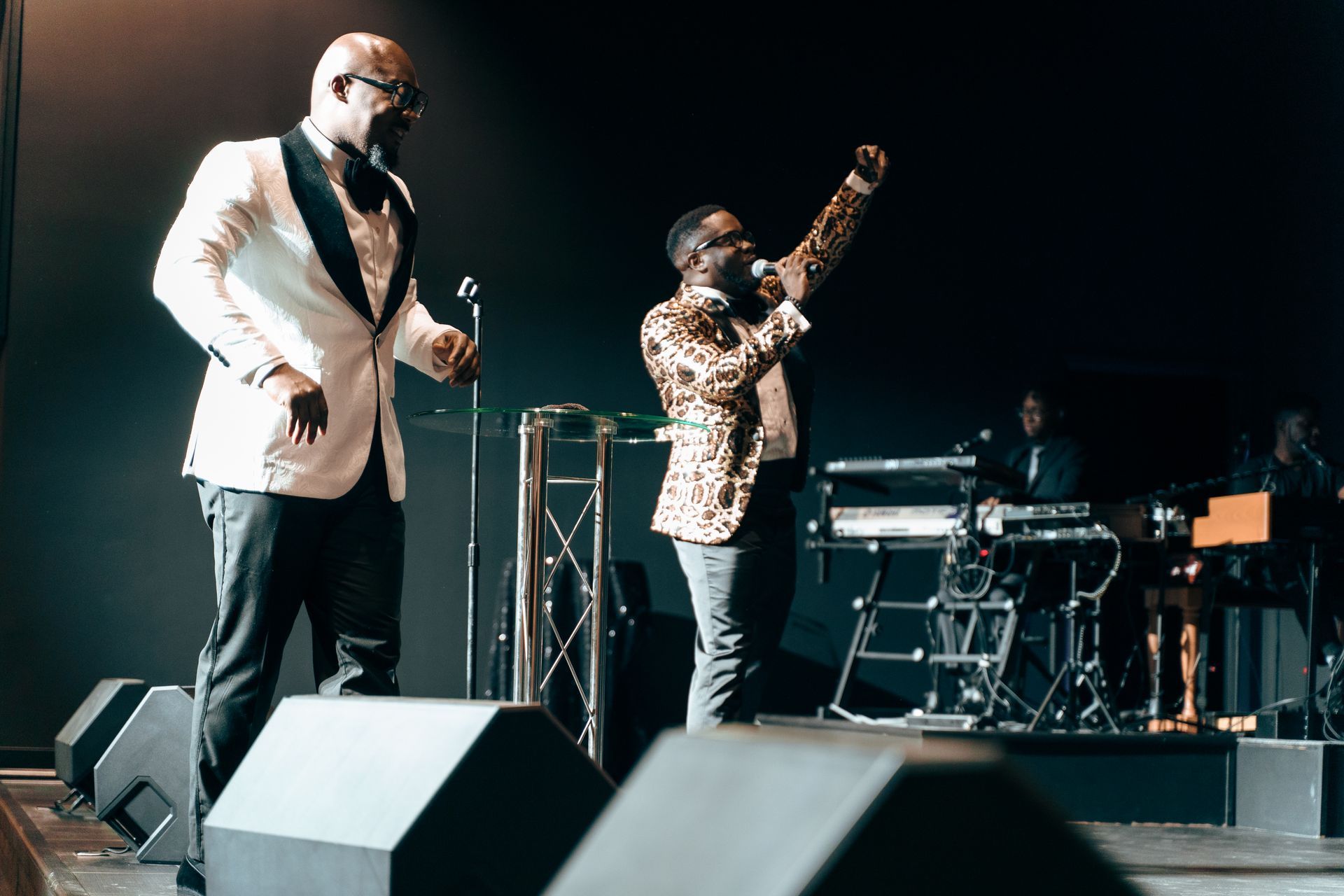 Two men are singing into microphones on a stage.