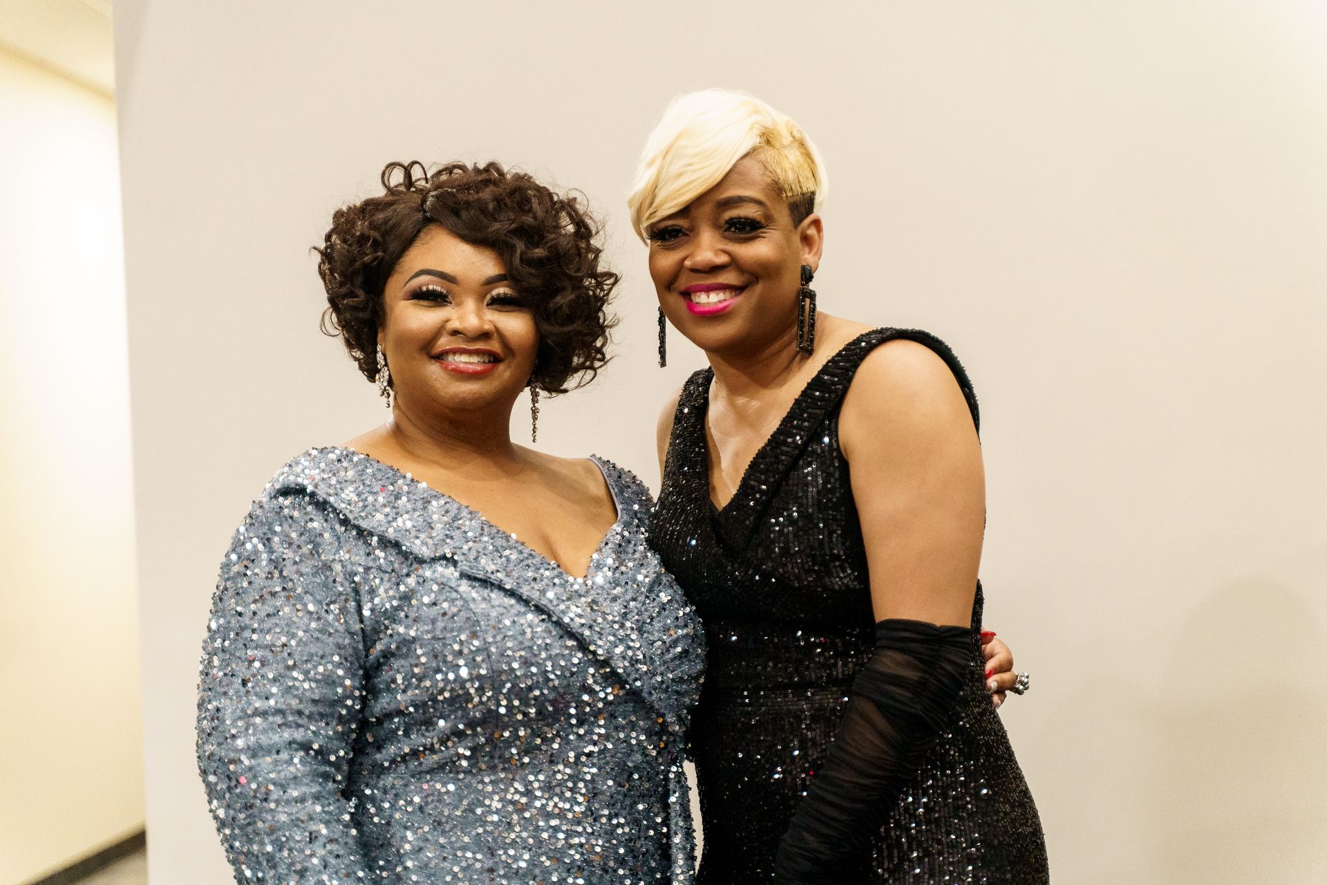 Two women in sequined dresses are posing for a picture.