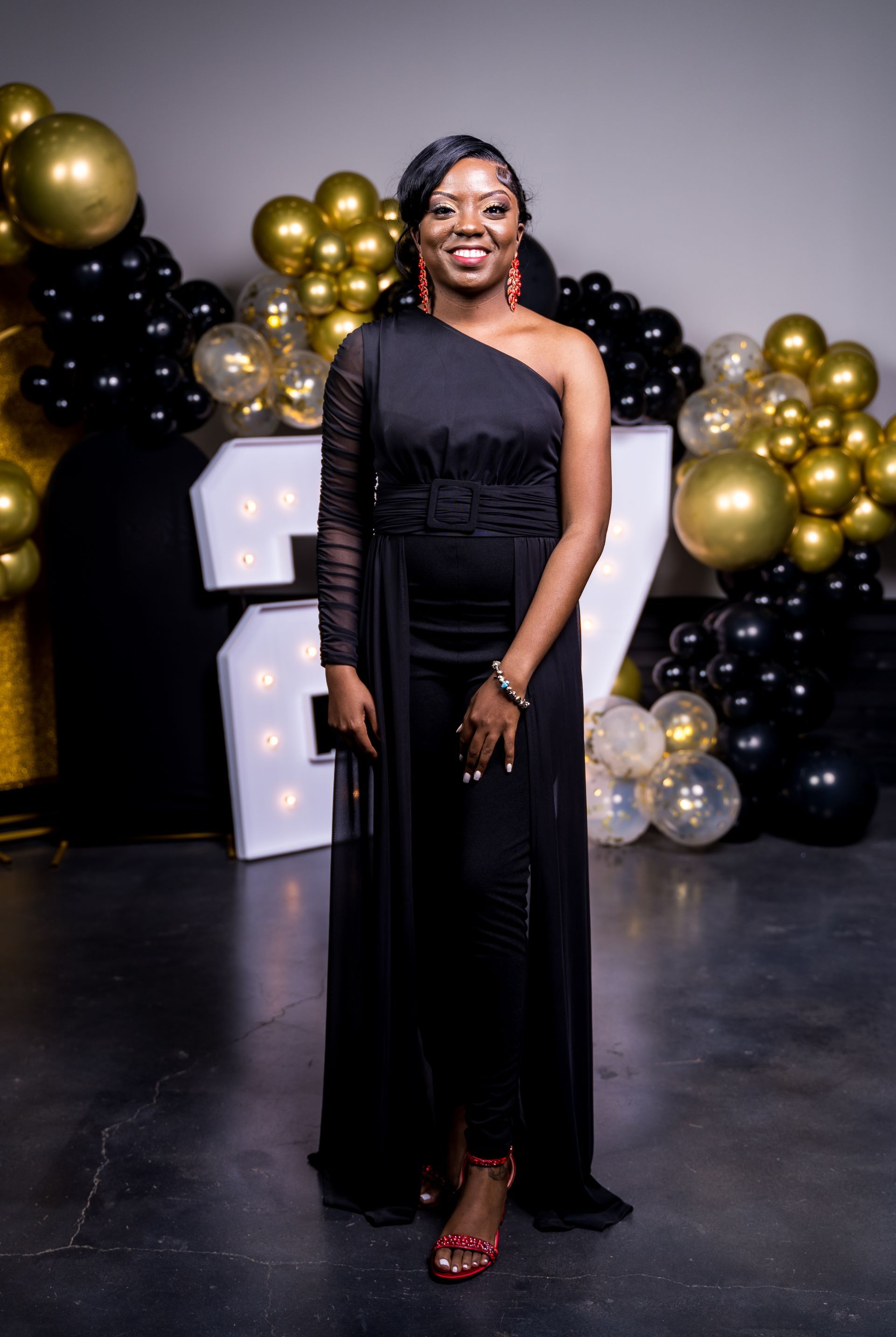 A woman in a black dress is standing in front of balloons.