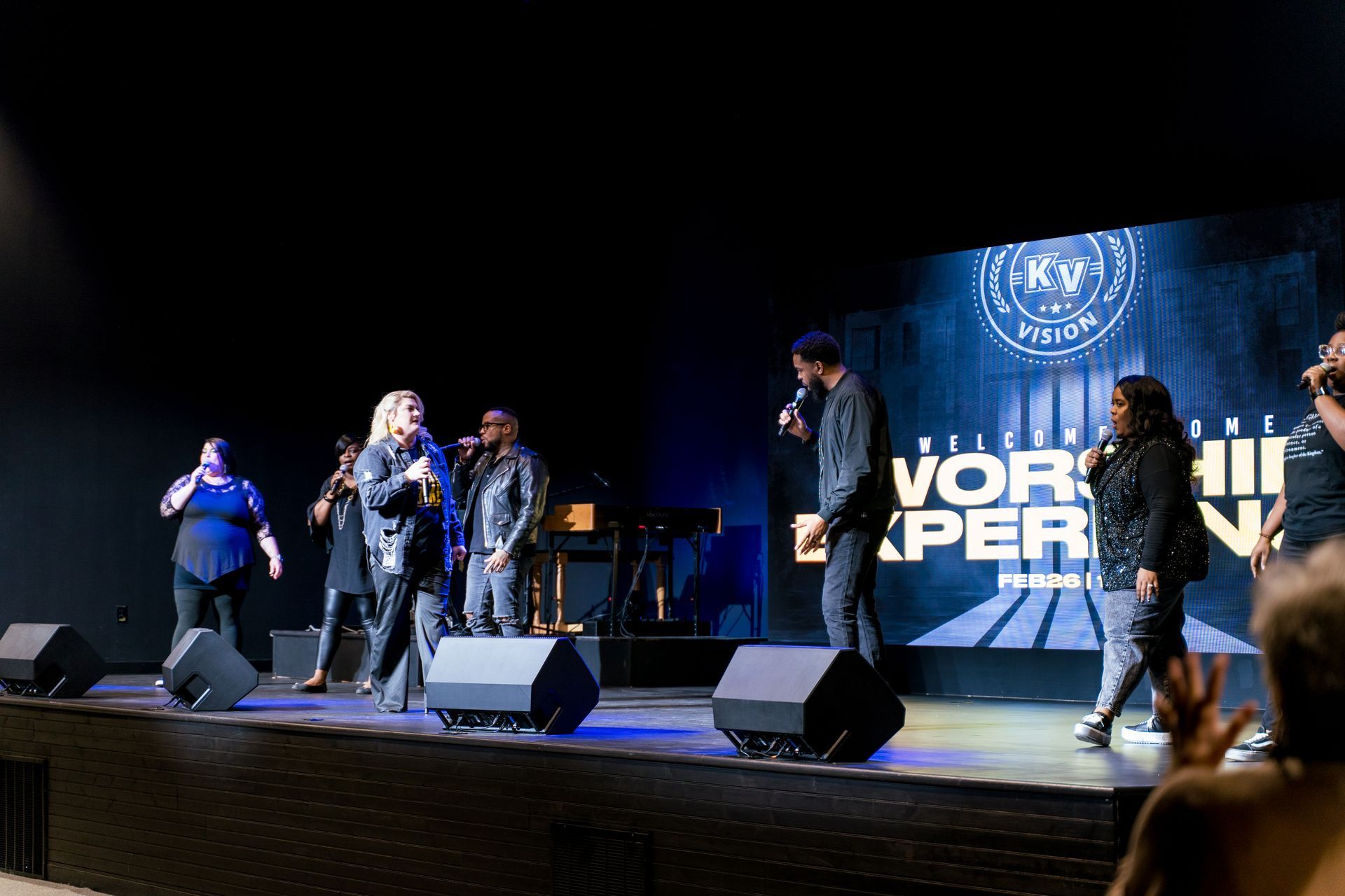 A group of people are singing on a stage in front of a large screen.