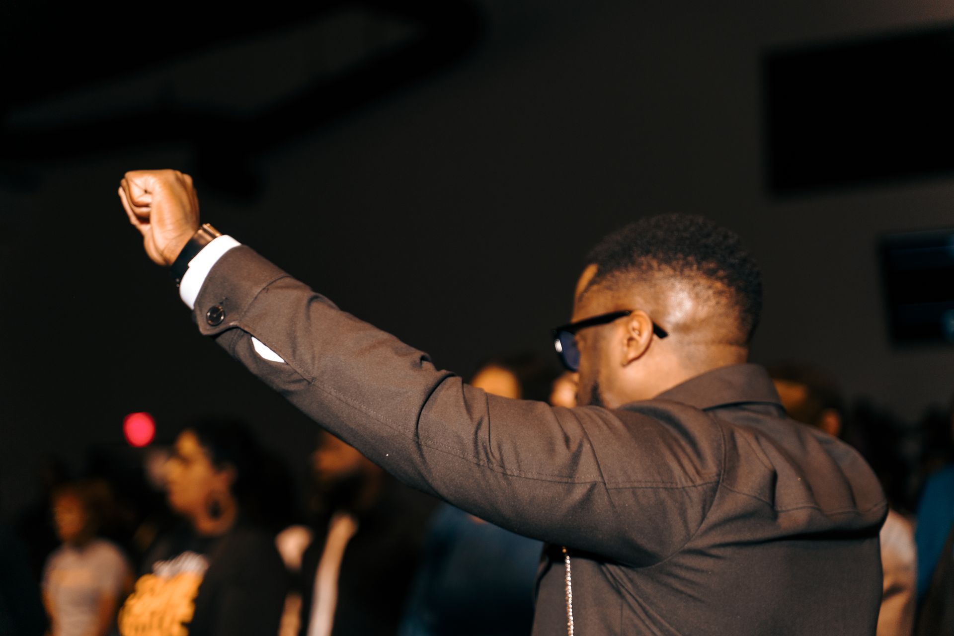 A man in a suit and glasses is raising his fist in the air.
