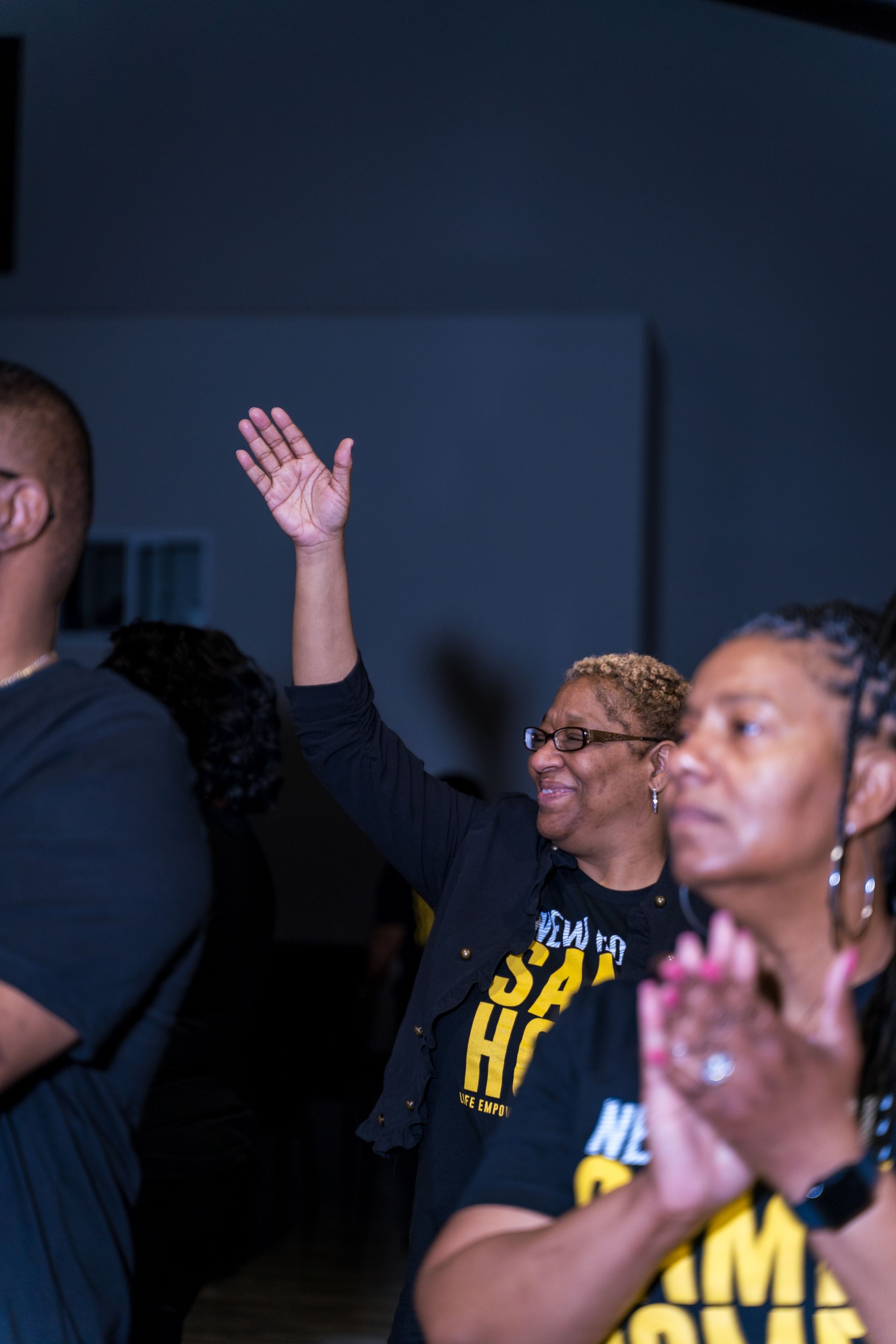 A group of people are clapping and one of them is wearing a shirt that says hi