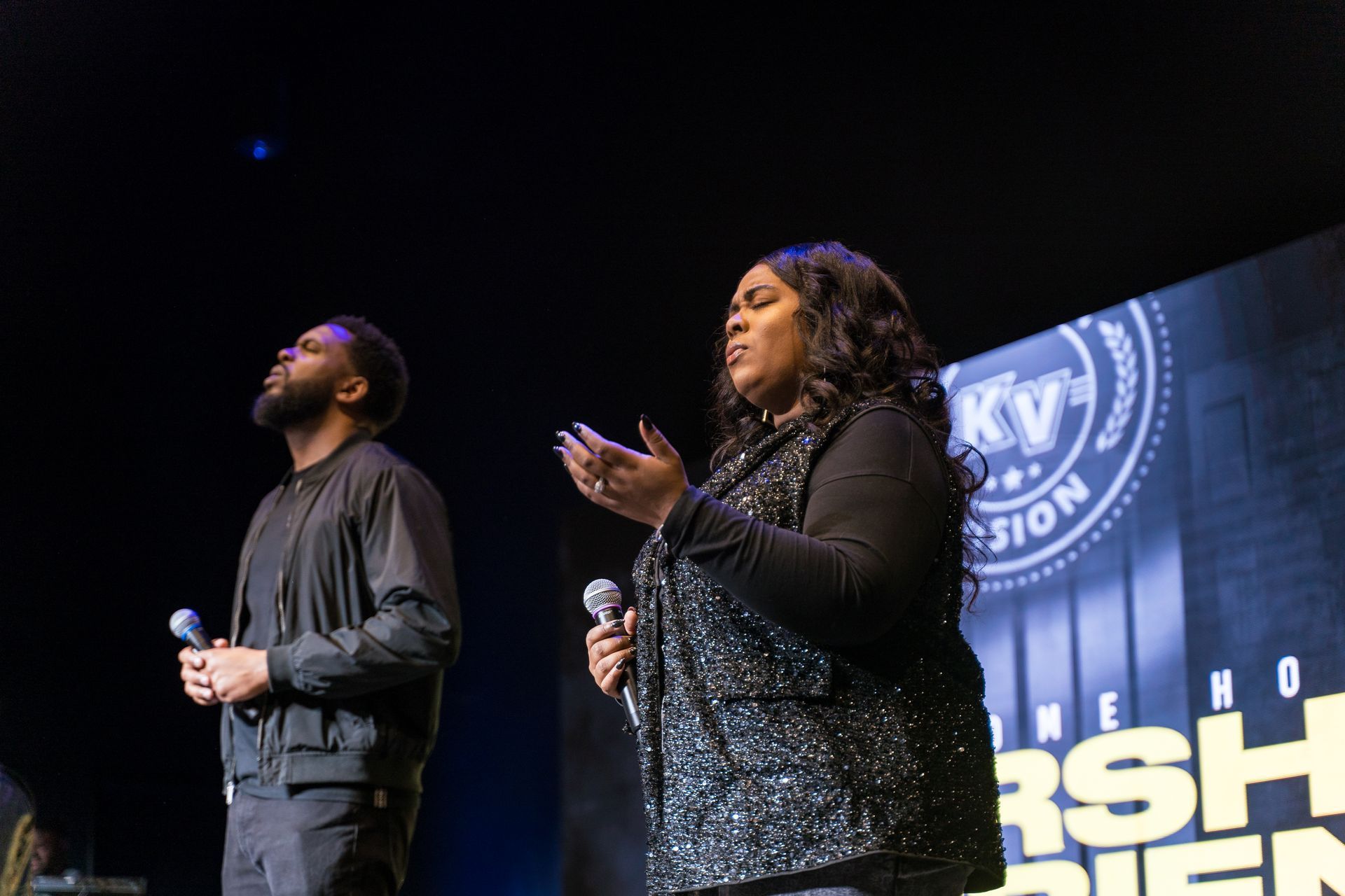 A man and a woman are singing into microphones on a stage.