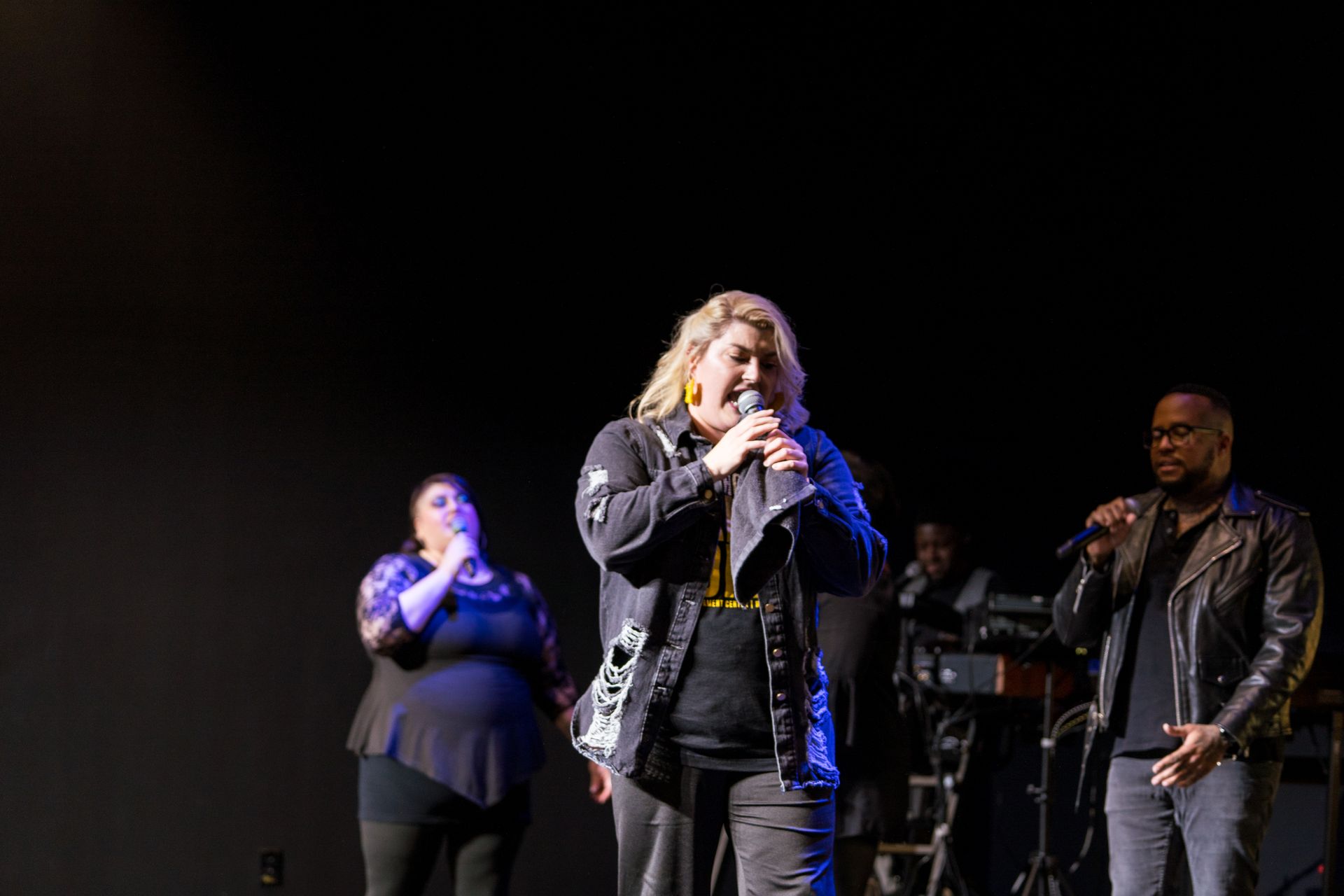 A group of people are singing into microphones on a stage.