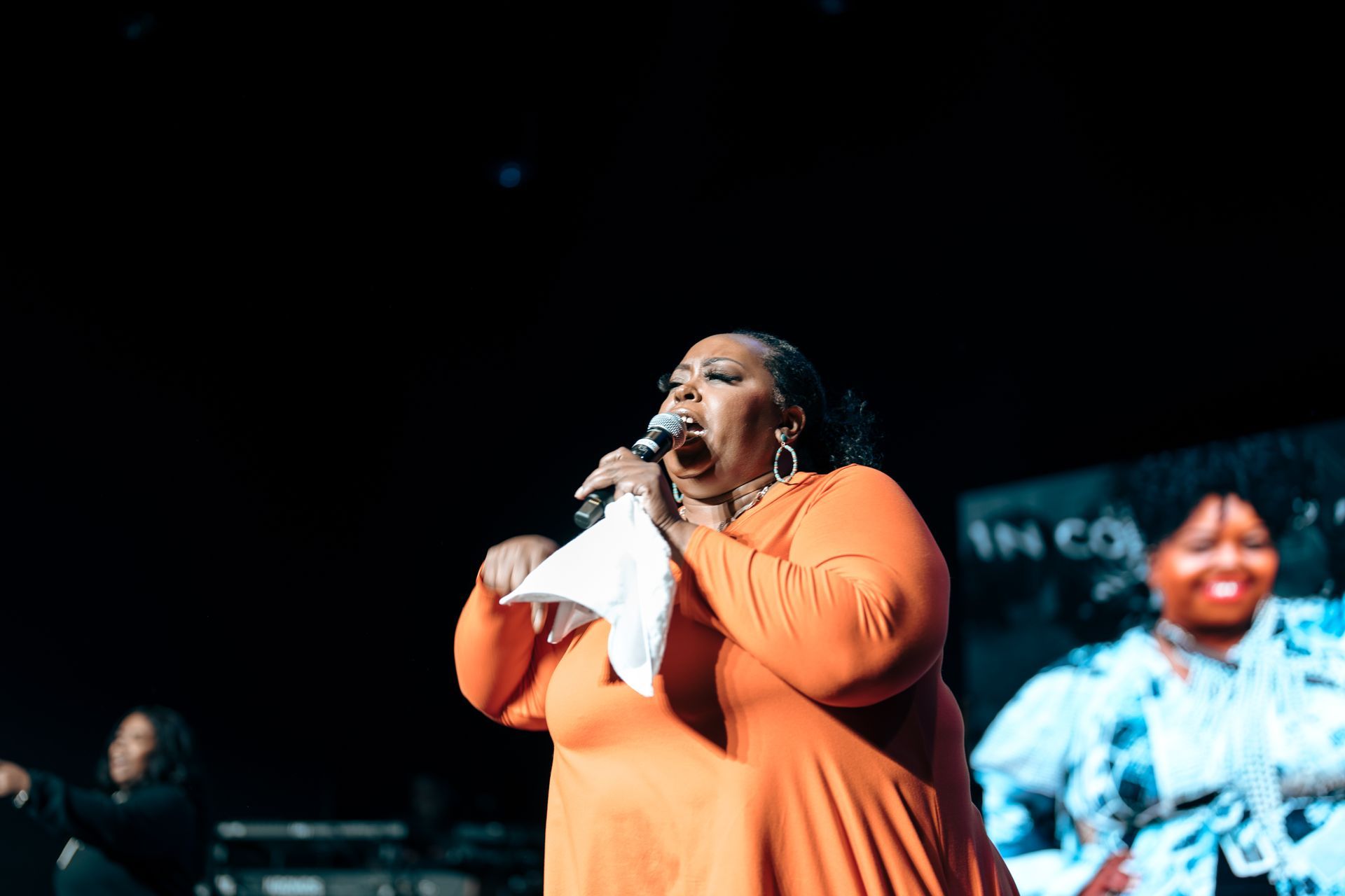 A woman in an orange dress is singing into a microphone on a stage.