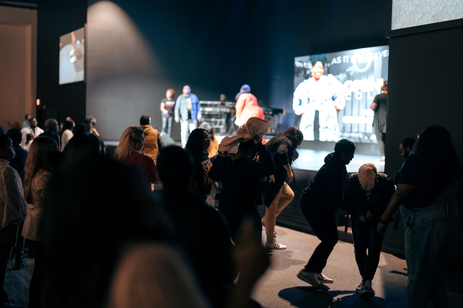 A group of people are dancing in front of a large screen.