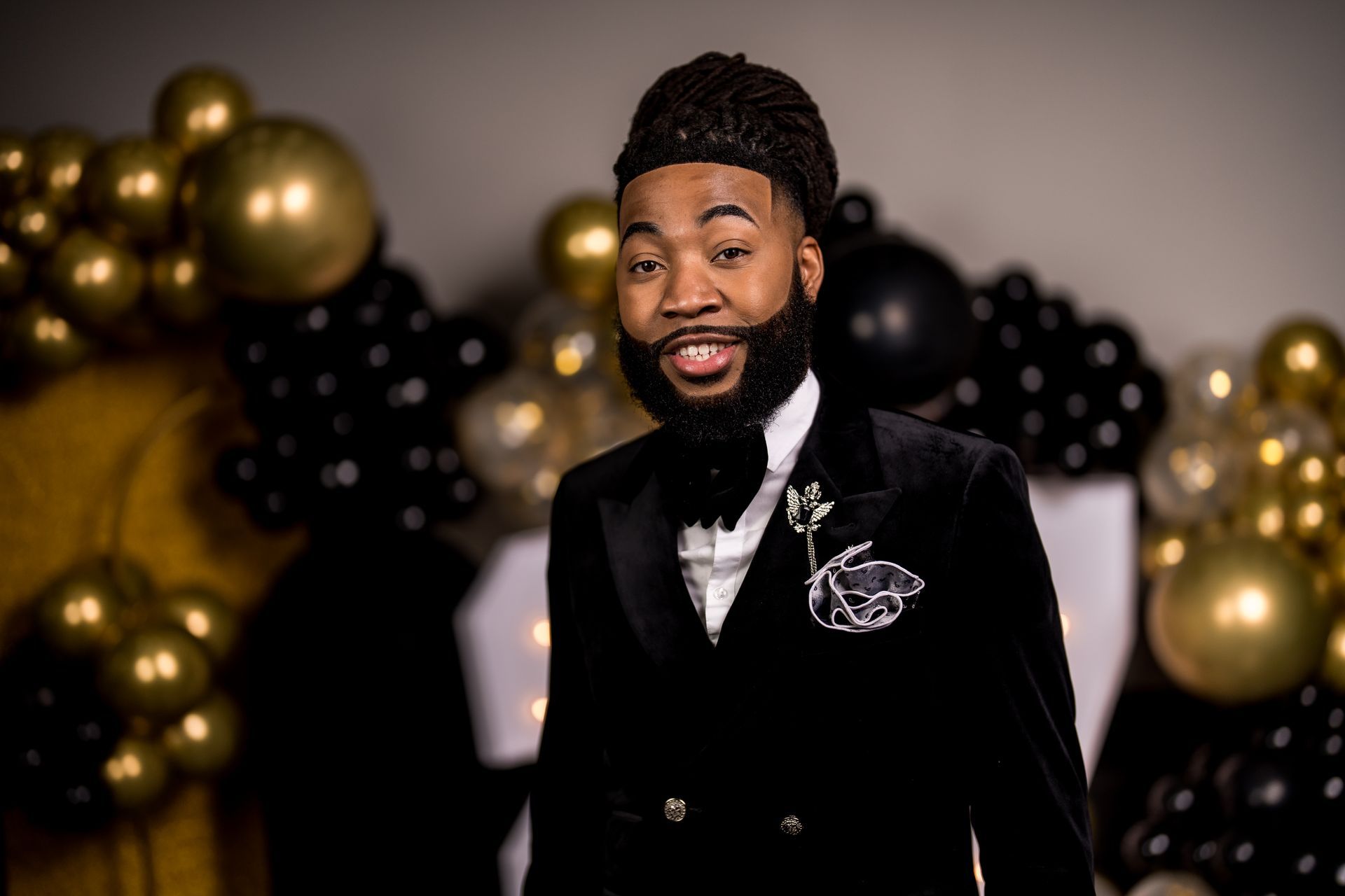A man in a tuxedo and bow tie is standing in front of balloons.