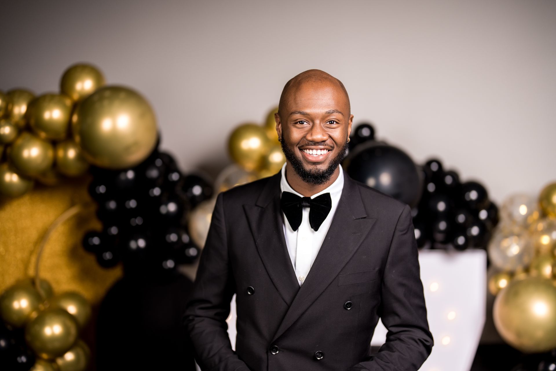 A man in a suit and bow tie is standing in front of balloons.