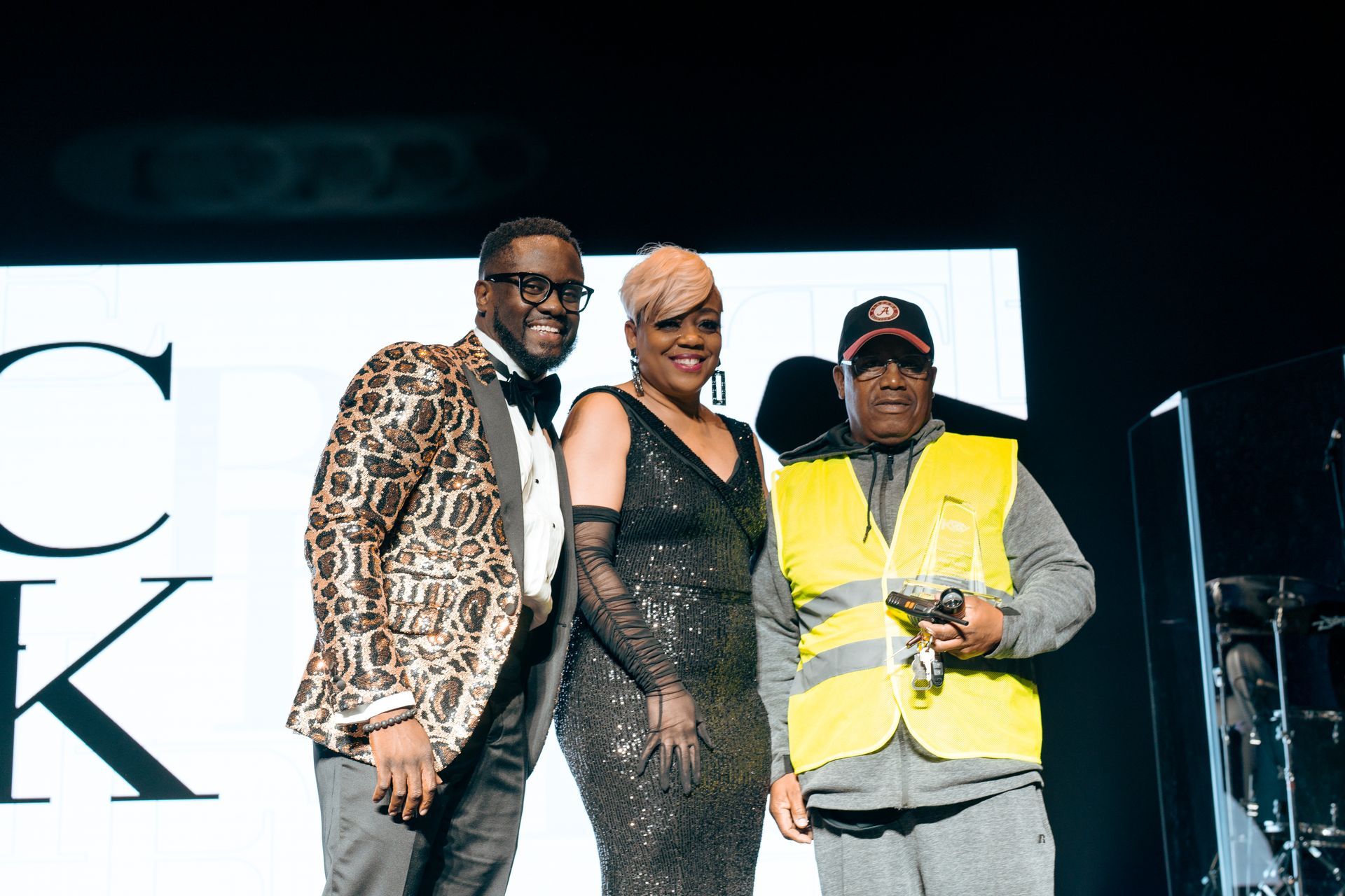 A man in a leopard print jacket is standing next to a woman in a black dress and a man in a yellow vest.