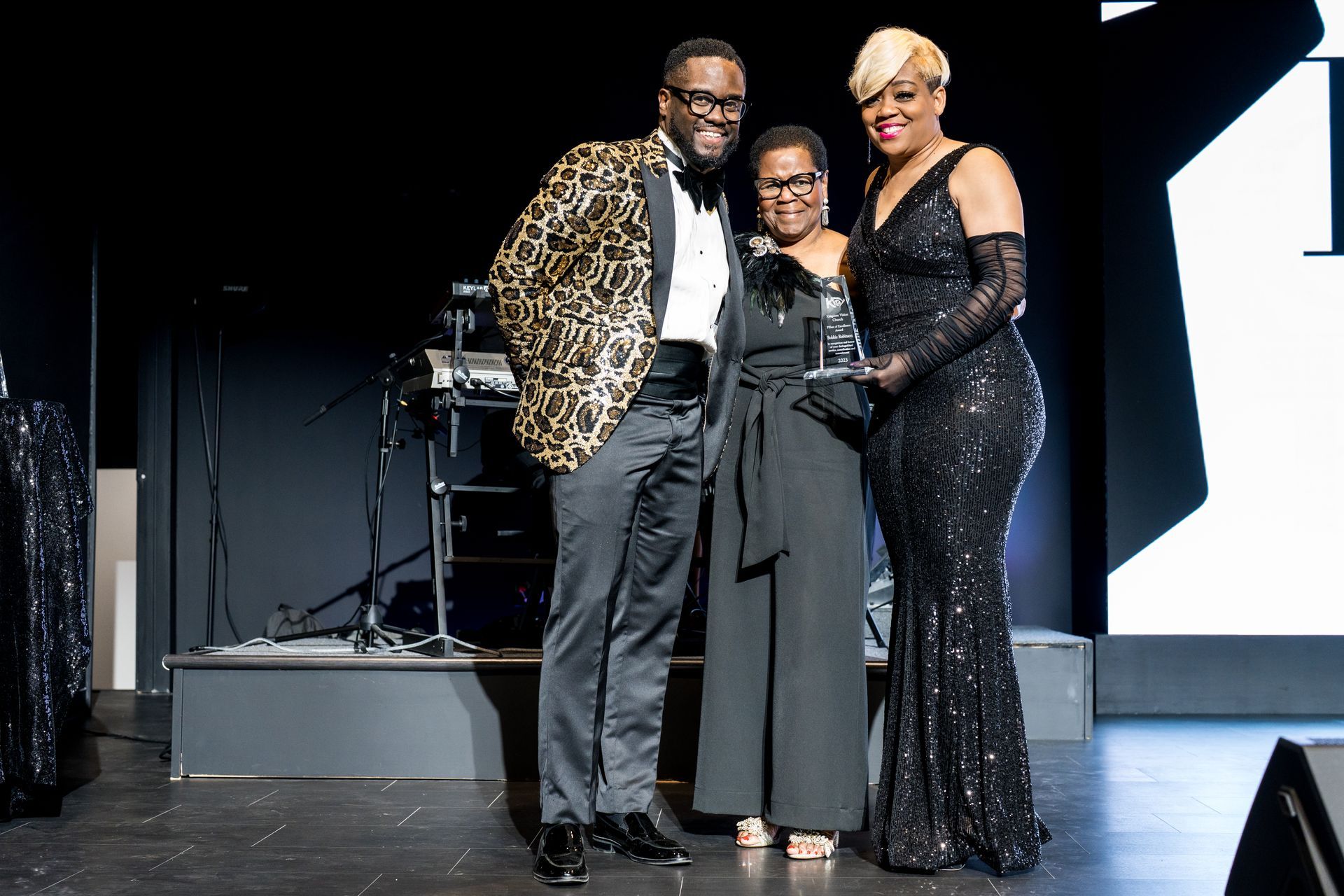 A man and two women are standing on a stage holding an award.